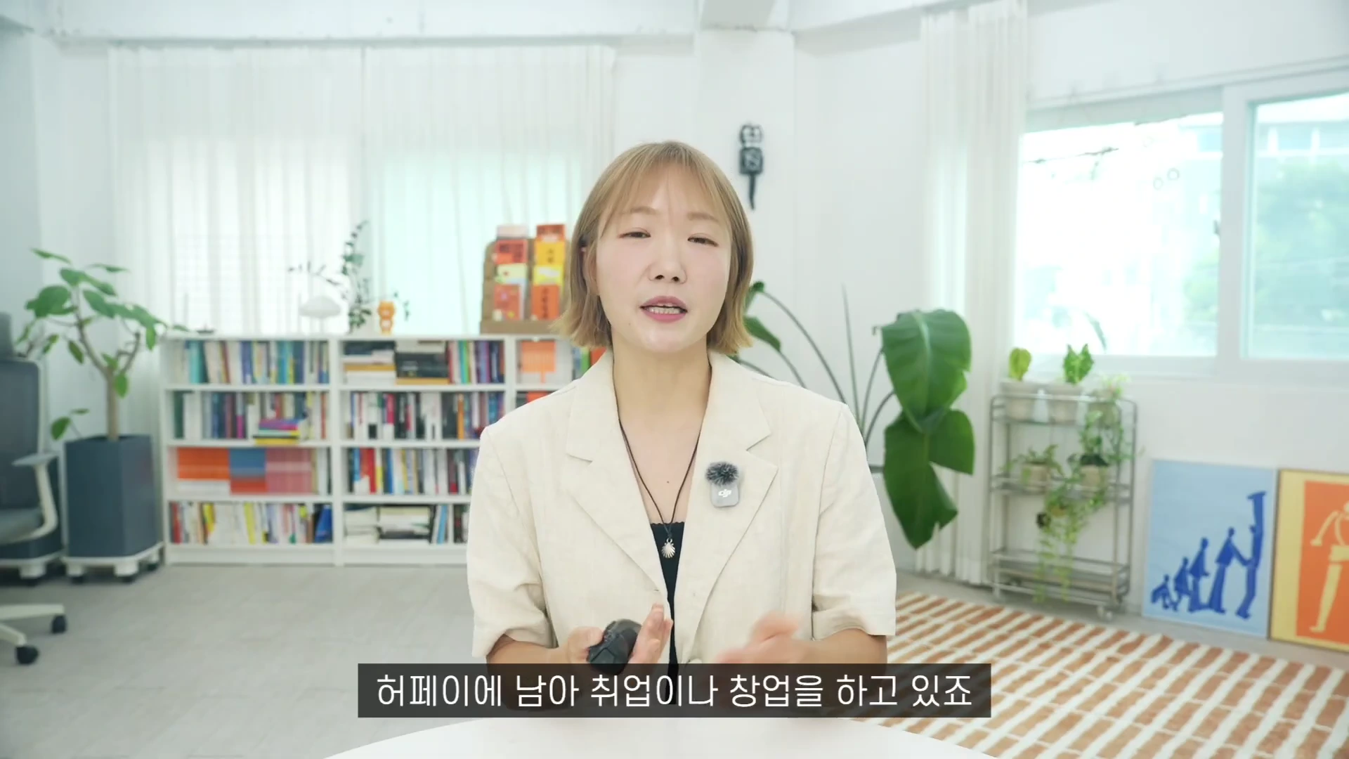 밝은 실내에서 단발머리의 여성 출연자가 책장이 있는 배경 앞에서 손짓을 하며 이야기를 나누고 있는 모습