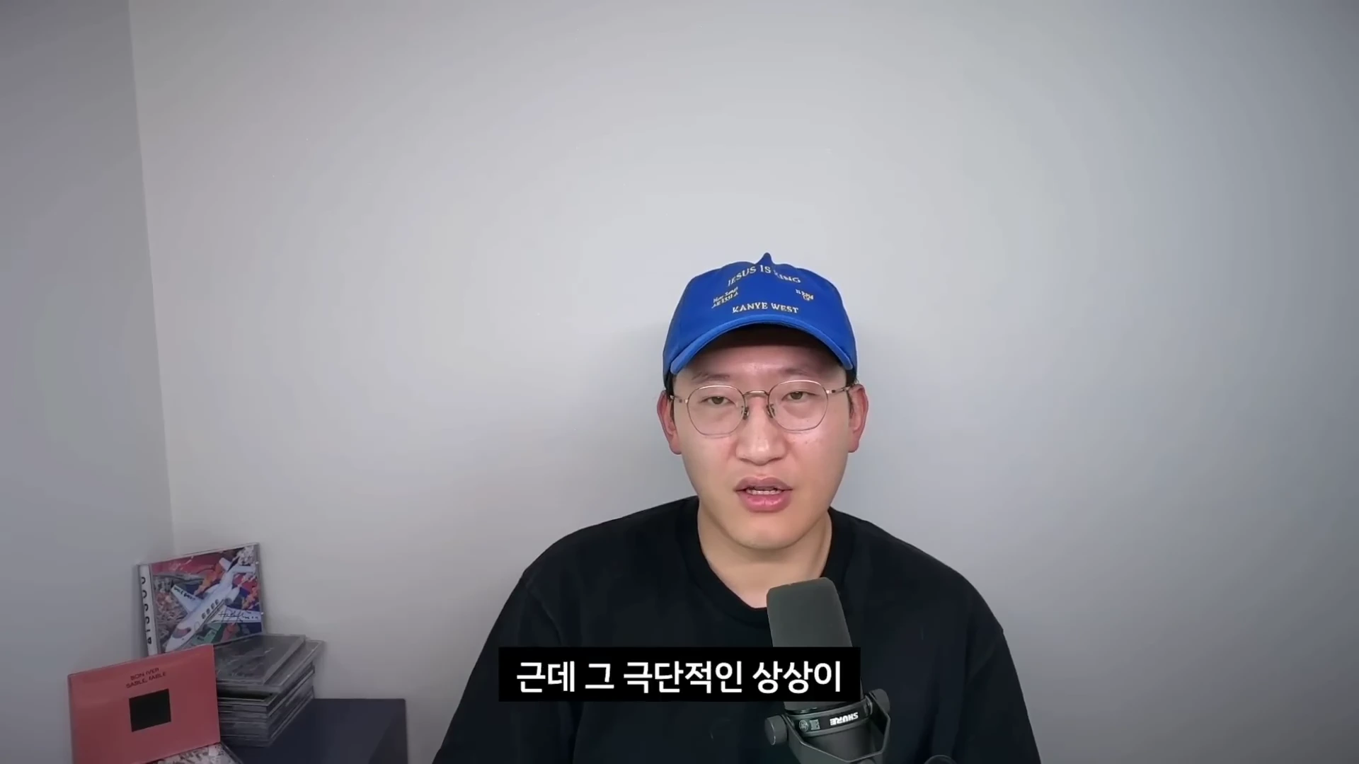 파란색 볼캡 모자와 안경을 쓴 남성이 마이크 앞에 앉아 정면을 응시하며 이야기하고 있고, 화면 하단에는 '근데 그 극단적인 상상이'라는 한글 자막이 적혀 있습니다.