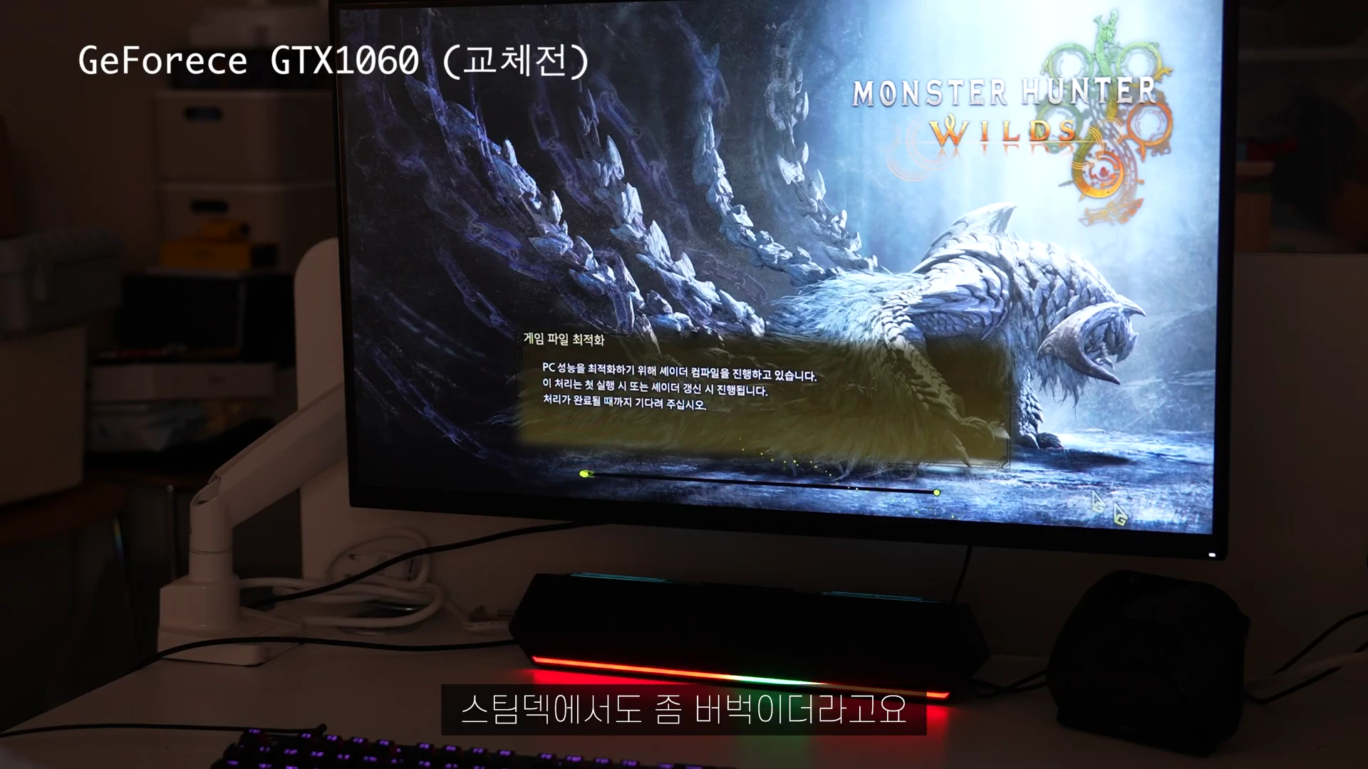 어두운 방 안의 모니터 화면에 '몬스터 헌터 와일즈' 게임 로딩 화면이 나타나 있고, 화면 상단에는 'GeForce GTX 1060 (교체전)'이라는 텍스트가 표시되어 있습니다.