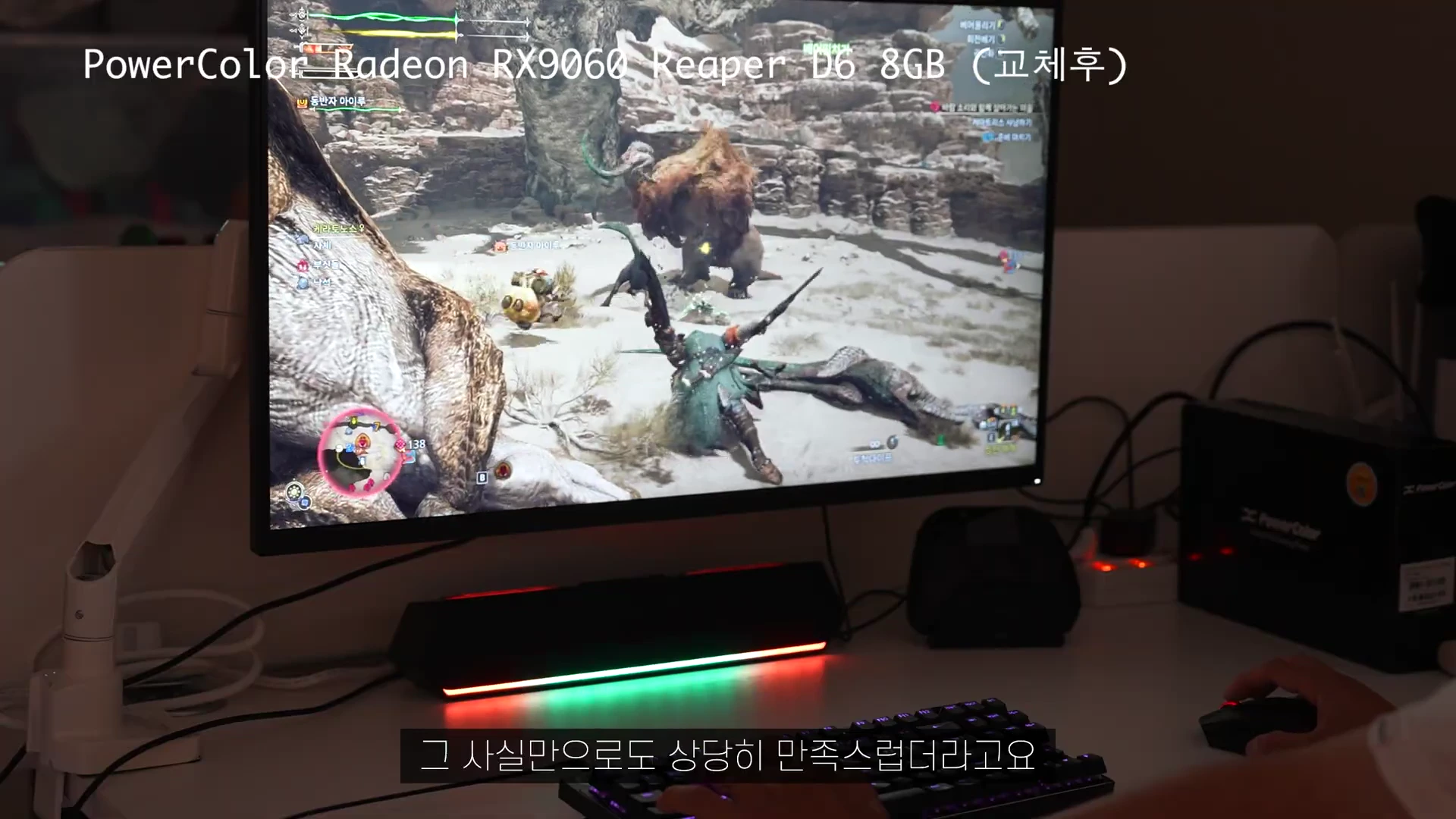 책상 위에 놓인 모니터에서 몬스터 헌터 와일즈 게임이 실행 중이며 상단에 그래픽 카드 모델명이 텍스트로 표시되어 있습니다.