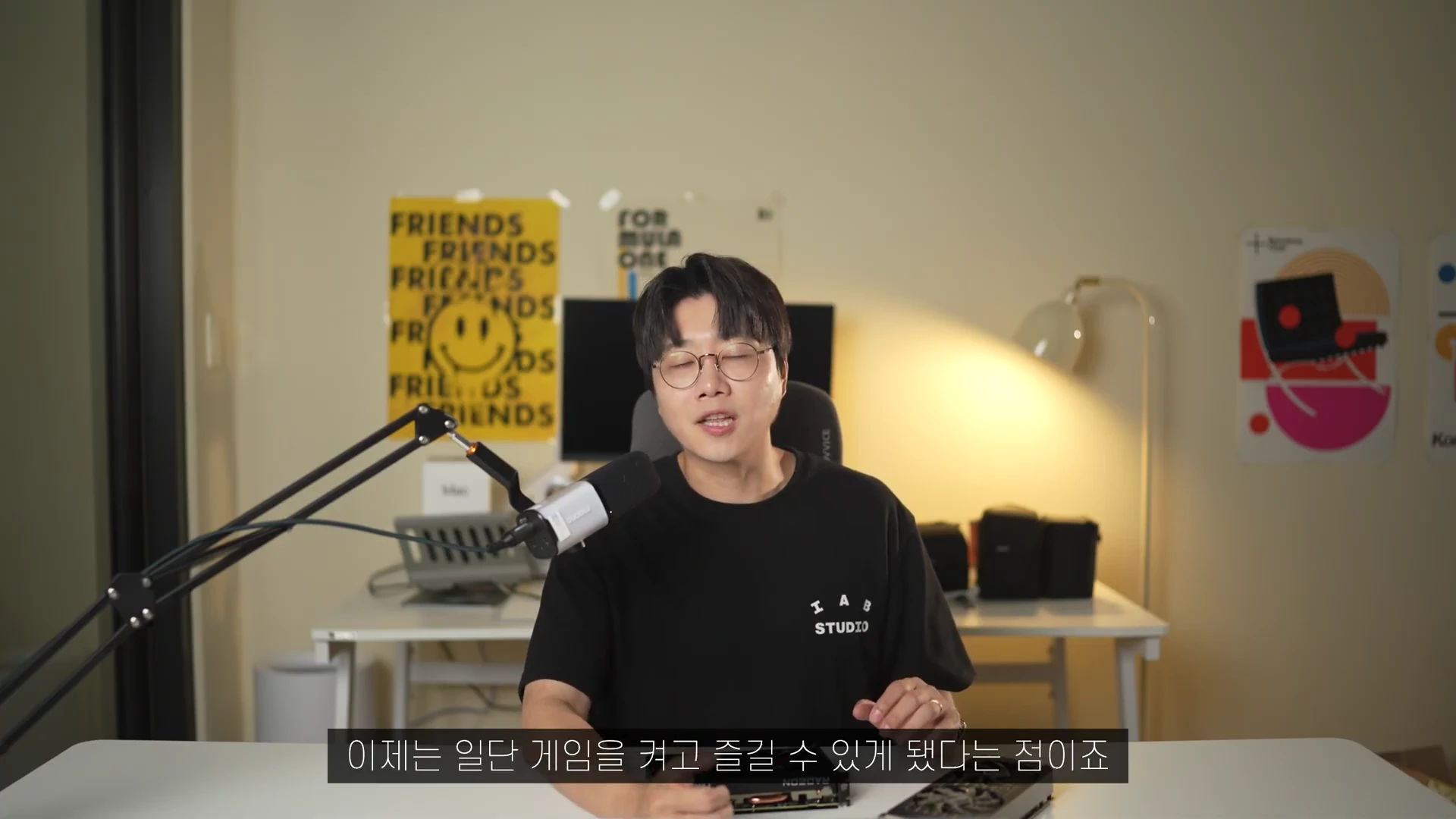 안경을 쓴 남성이 책상 앞에 앉아 마이크를 앞에 두고 이야기를 나누고 있는 모습으로, 하단에는 한글 자막이 떠 있습니다.