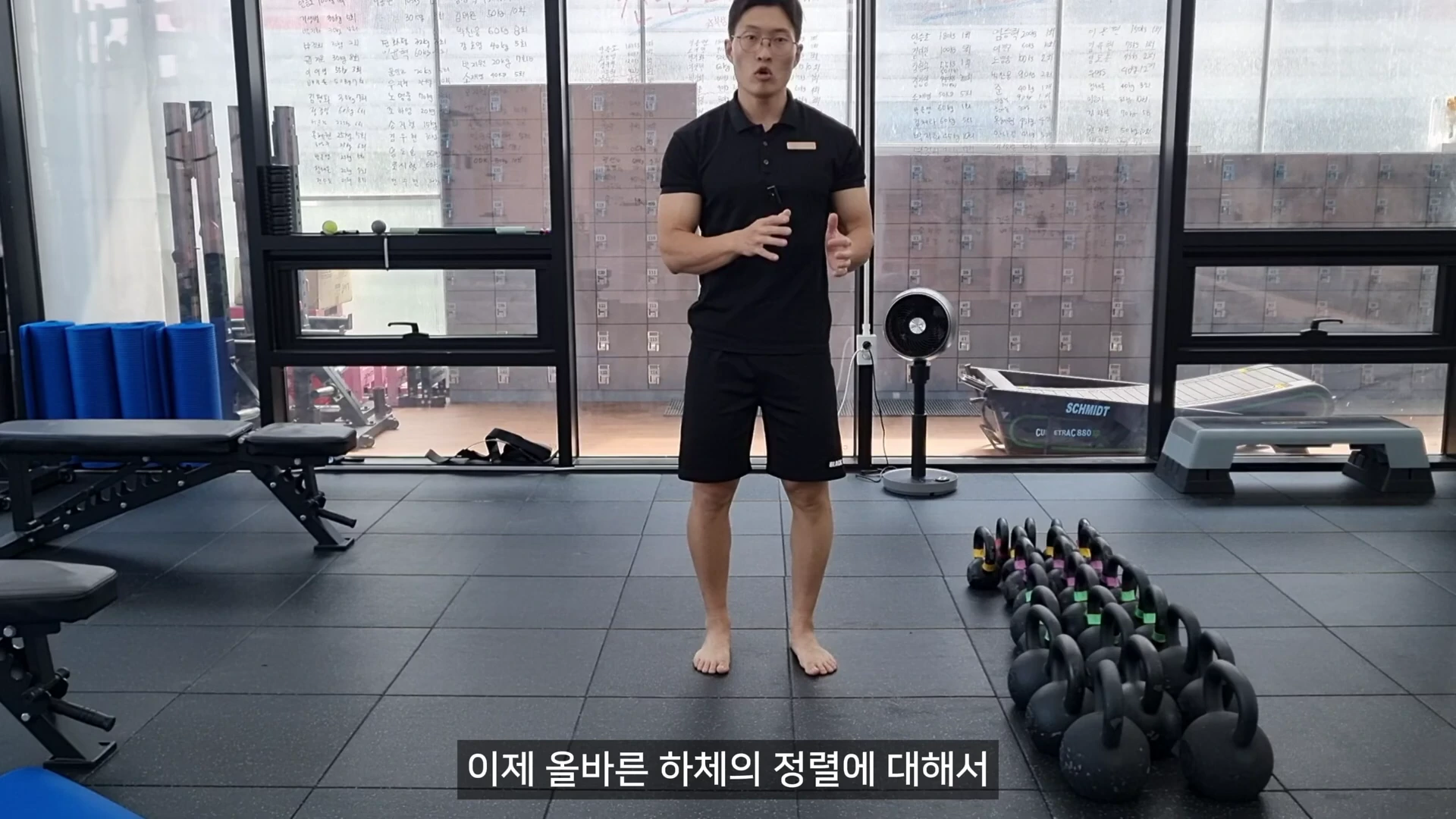 운동복을 입은 남성이 피트니스 센터에서 맨발로 서서 손동작을 하며 설명을 하고 있는 모습