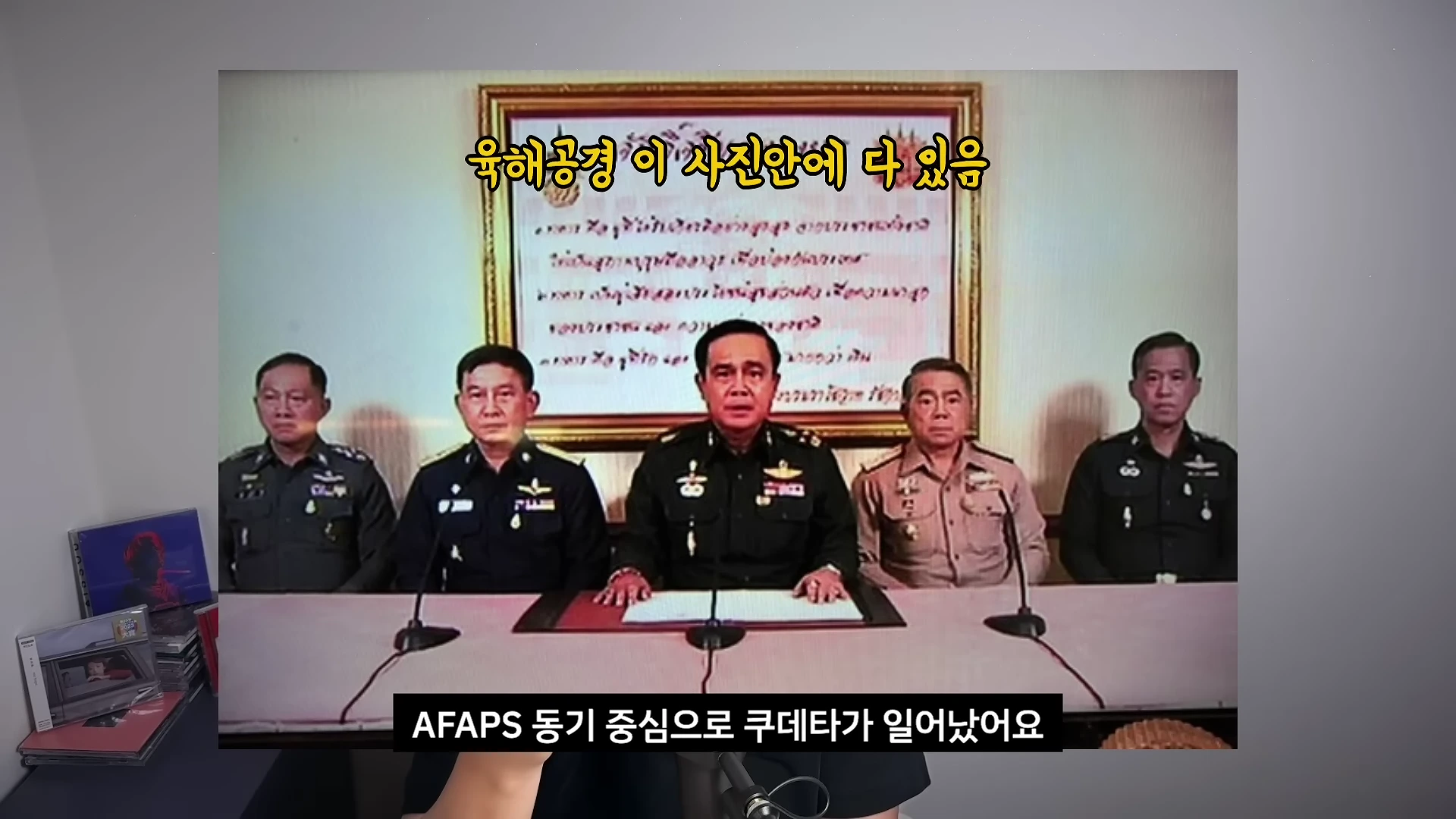 군복을 입은 5명의 남성이 테이블 앞에 앉아 있는 모습이 담긴 영상 속 화면이며, 하단에는 한국어 자막이 표시되어 있습니다.