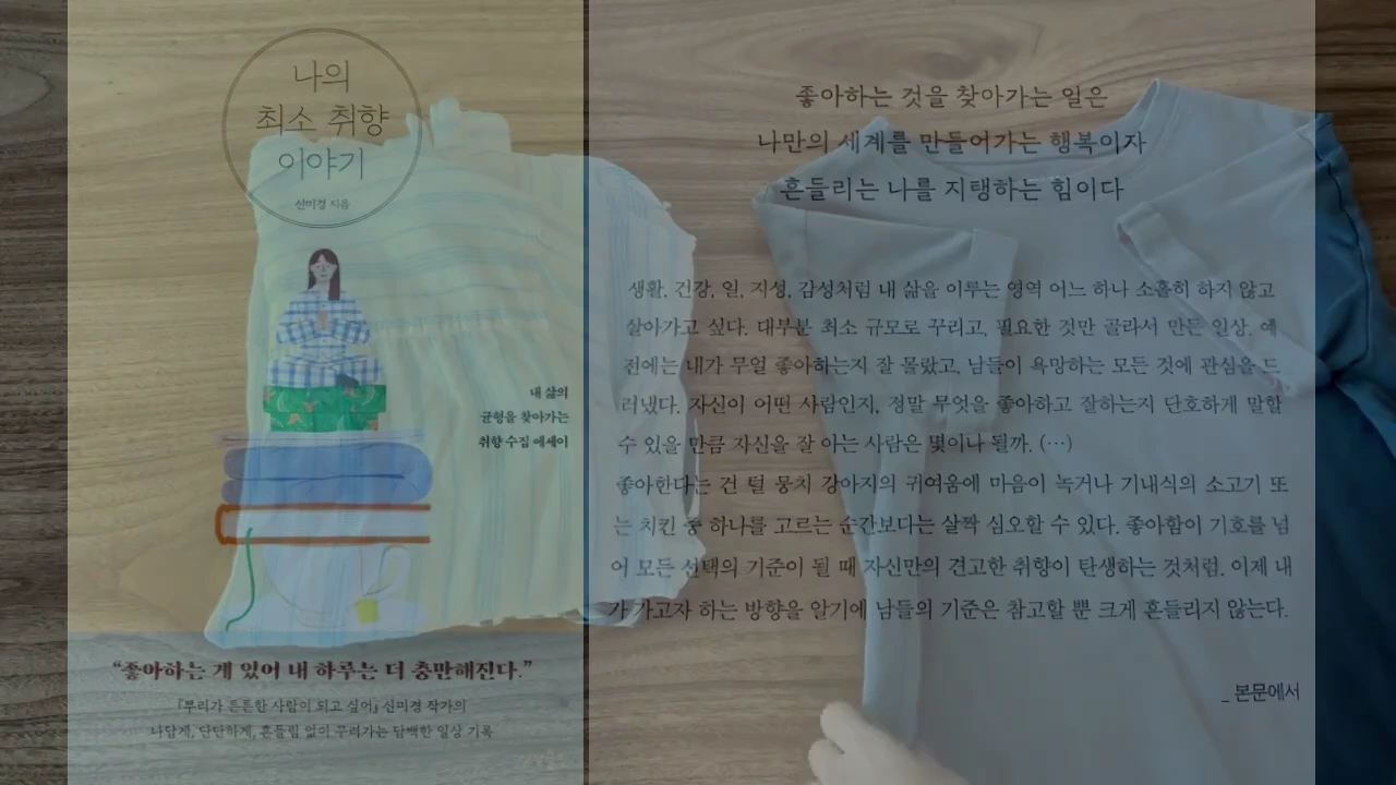 책 표지가 왼쪽, 텍스트가 적힌 흰색 티셔츠가 오른쪽에 놓여 있고 그 위로 손이 살짝 얹혀 있는 모습