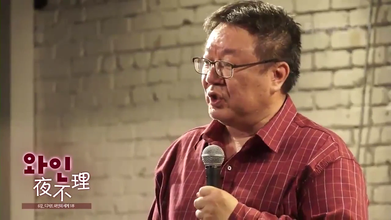 안경을 쓰고 붉은 체크무늬 셔츠를 입은 남성이 마이크를 잡고 강연하는 모습