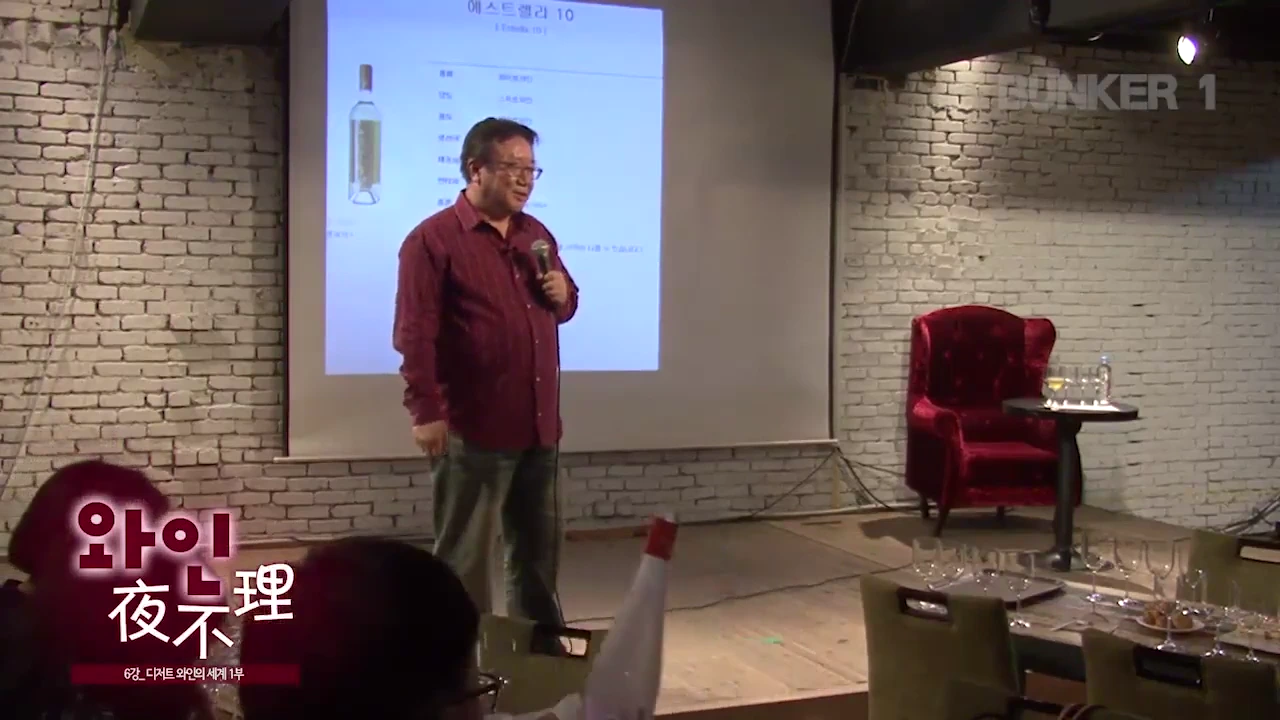 강연자가 무대 위에서 마이크를 잡고 서 있고, 뒤편 스크린에는 '에스트렐라 10' 와인 정보가 담긴 슬라이드가 투사되어 있다.