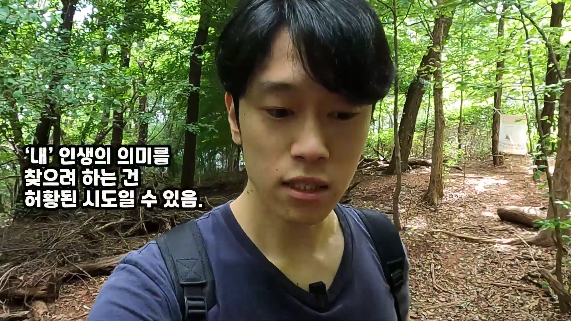 숲길을 걷고 있는 한 남성이 카메라를 보며 이야기하고 있고, 화면 왼쪽에는 '내 인생의 의미를 찾으려 하는 건 허황된 시도일 수 있음'이라는 자막이 떠 있습니다.
