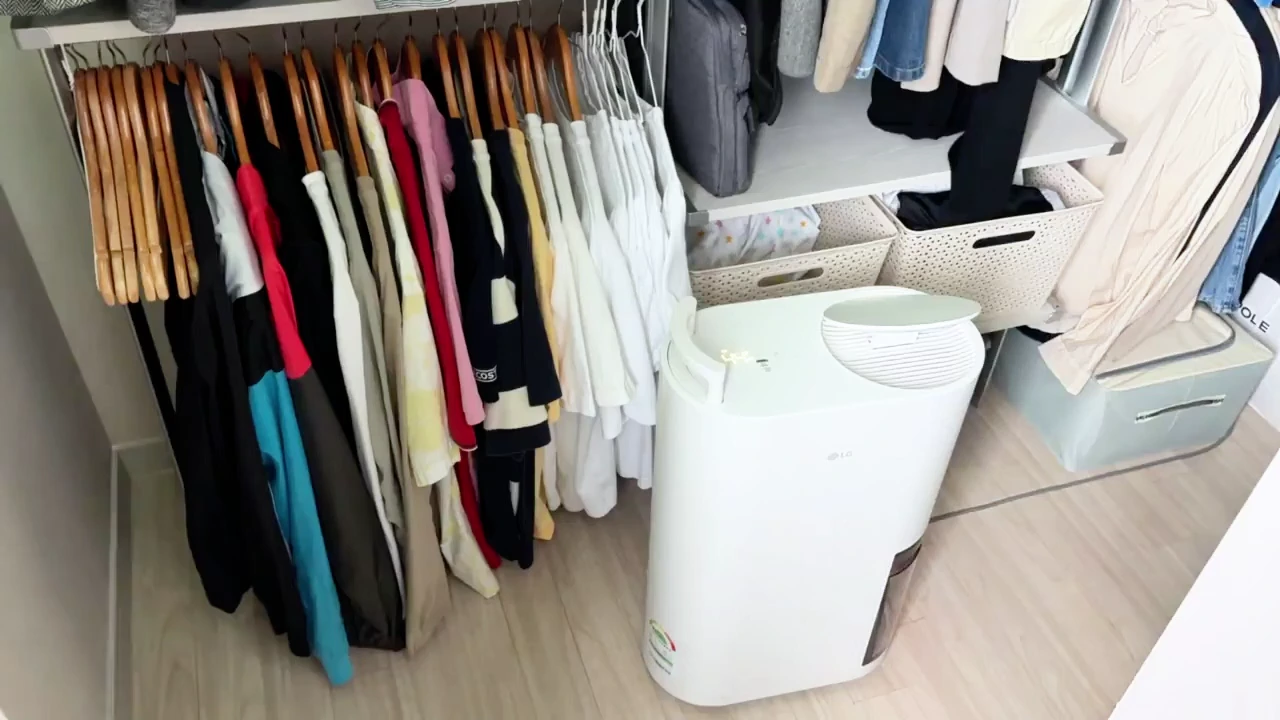 드레스룸 옷걸이에 걸린 옷들 옆에 하얀색 제습기가 놓여 있는 모습