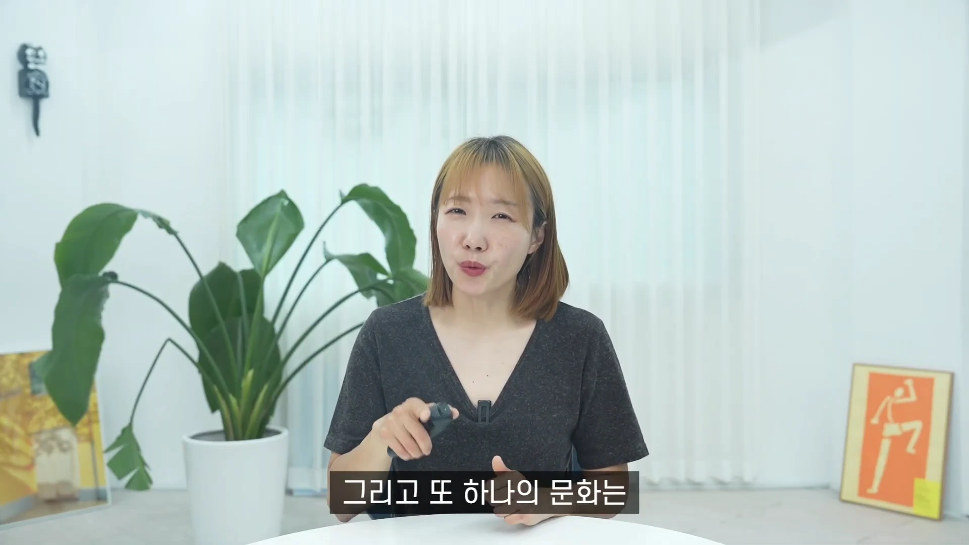 밝은 실내를 배경으로 책상 앞에 앉아 이야기하는 단발머리 여성. 화면 하단에는 '그리고 또 하나의 문화는'이라는 자막이 떠 있다.