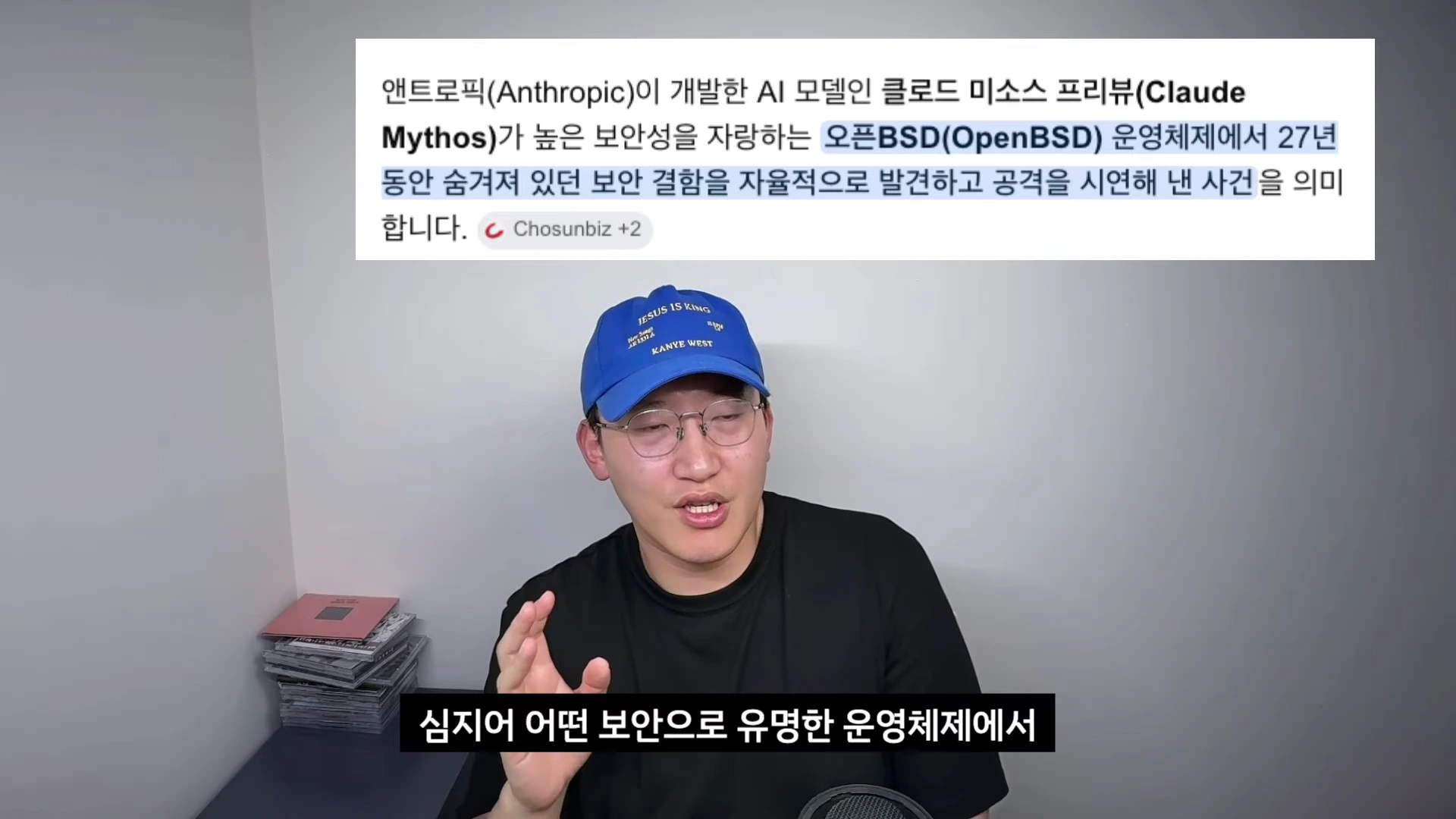 파란색 야구 모자를 쓴 남성이 카메라를 향해 이야기를 하고 있으며, 머리 위 화면에는 클로드 미소스 모델이 오픈BSD 운영체제의 보안 결함을 발견했다는 내용의 기사 요약 문구가 떠 있다.