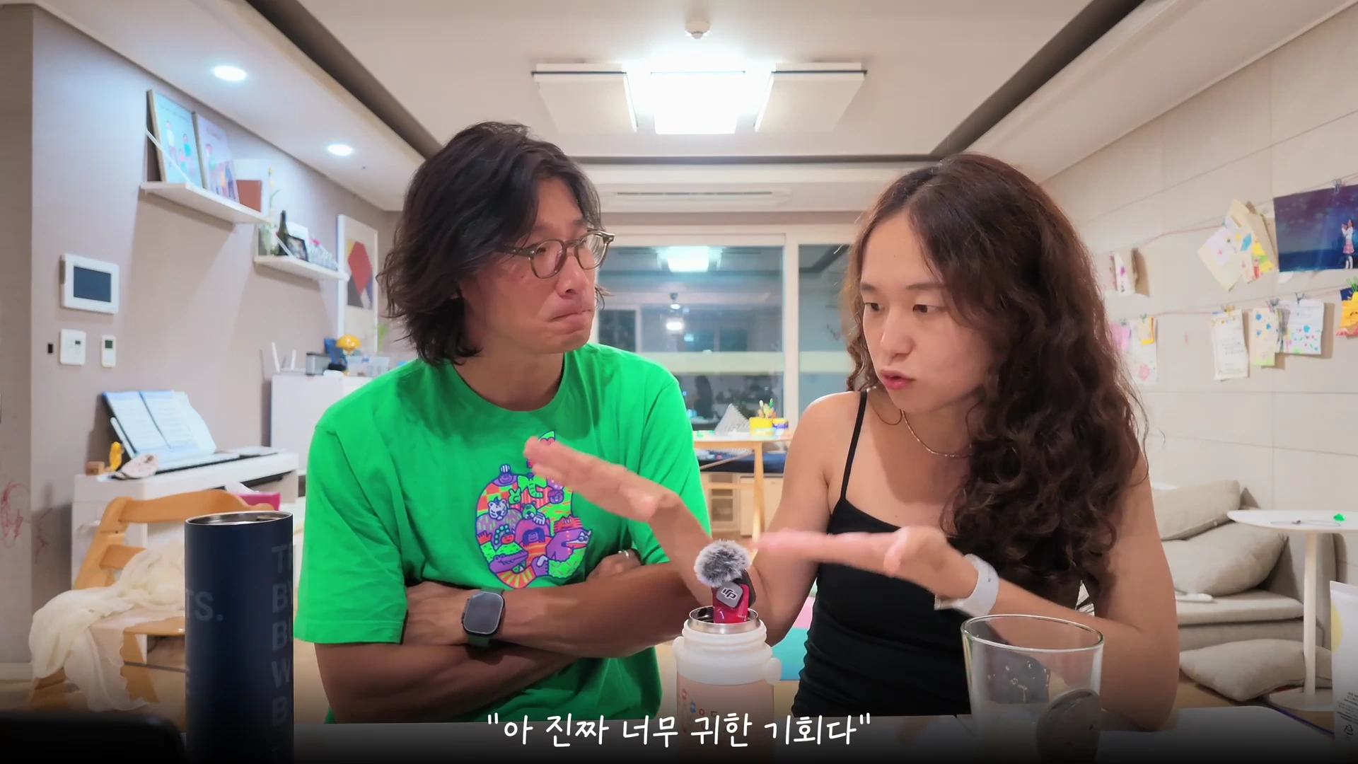 가정집 거실에 앉아 마이크를 앞에 두고 대화를 나누는 부부의 모습