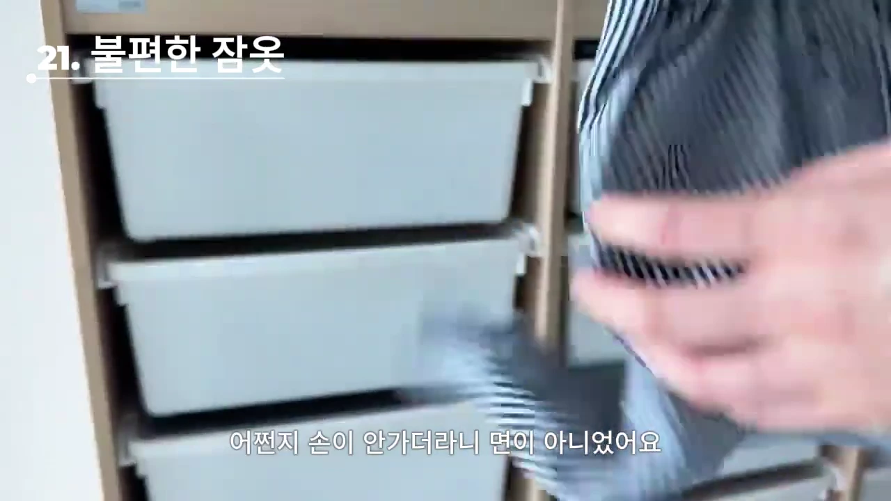 흰색 서랍장이 있는 배경에서 한 손이 줄무늬 잠옷 바지를 들고 있는 모습과 함께 '21. 불편한 잠옷'이라는 자막이 화면 상단에 표시되어 있다.