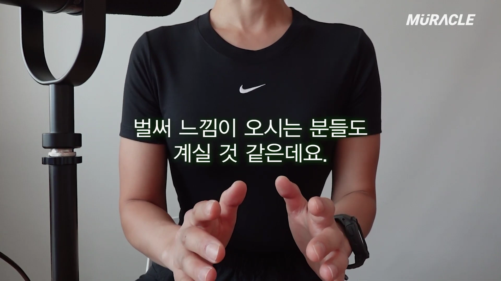검은색 반팔 티셔츠를 입고 마이크 앞에서 손동작하며 이야기하는 사람의 상반신 모습과 화면 중앙의 한국어 자막.
