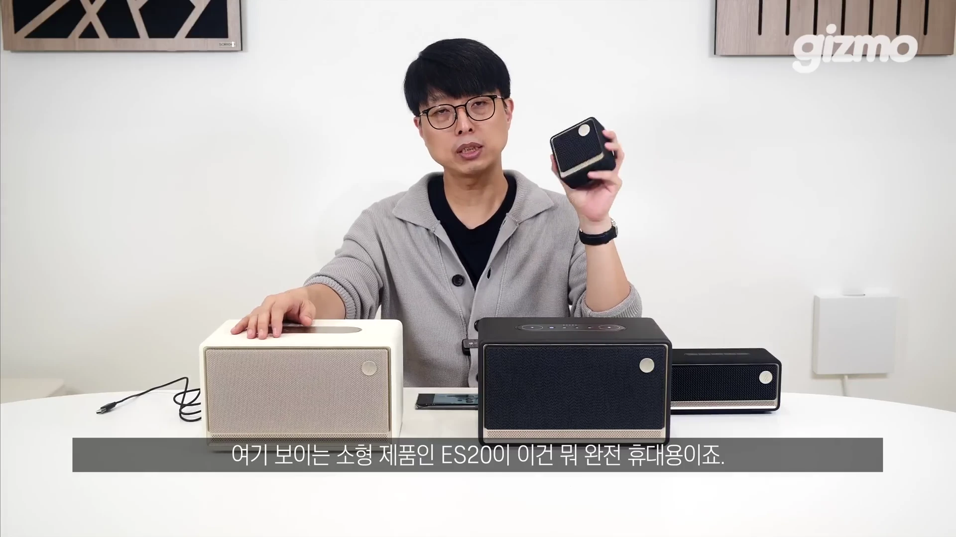 안경을 쓴 남성이 스튜디오 테이블 위에 놓인 다양한 크기의 에디파이어 스피커들과 손에 든 작은 스피커를 보여주고 있는 모습
