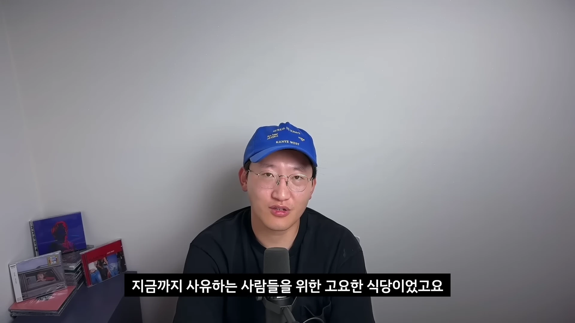 파란색 야구 모자와 안경을 쓴 남성이 마이크 앞에서 이야기하고 있는 모습의 정면 영상 캡처 화면.