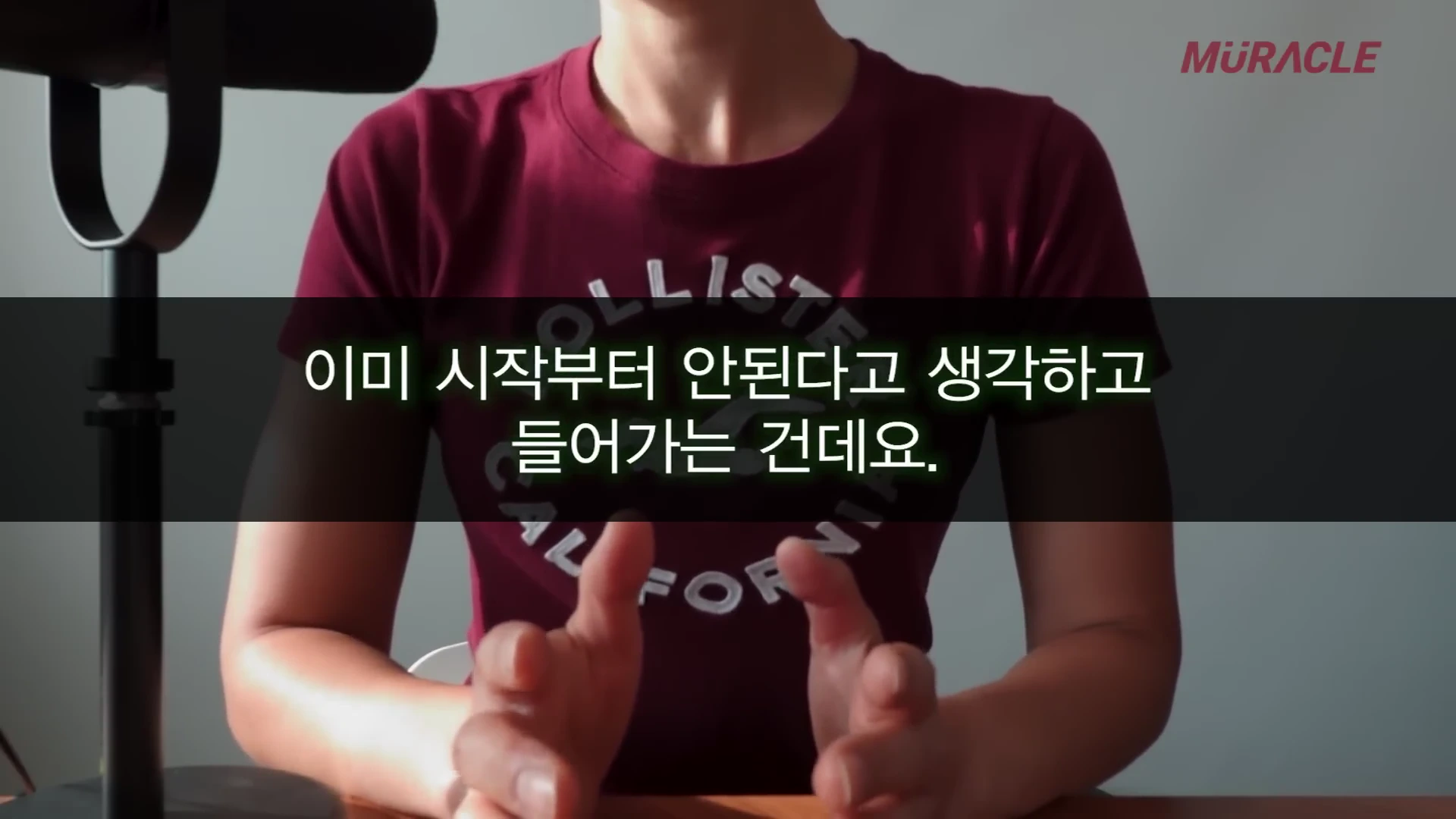 붉은색 반팔 티셔츠를 입고 의자에 앉아 손을 모으고 이야기하는 사람의 상반신 모습
