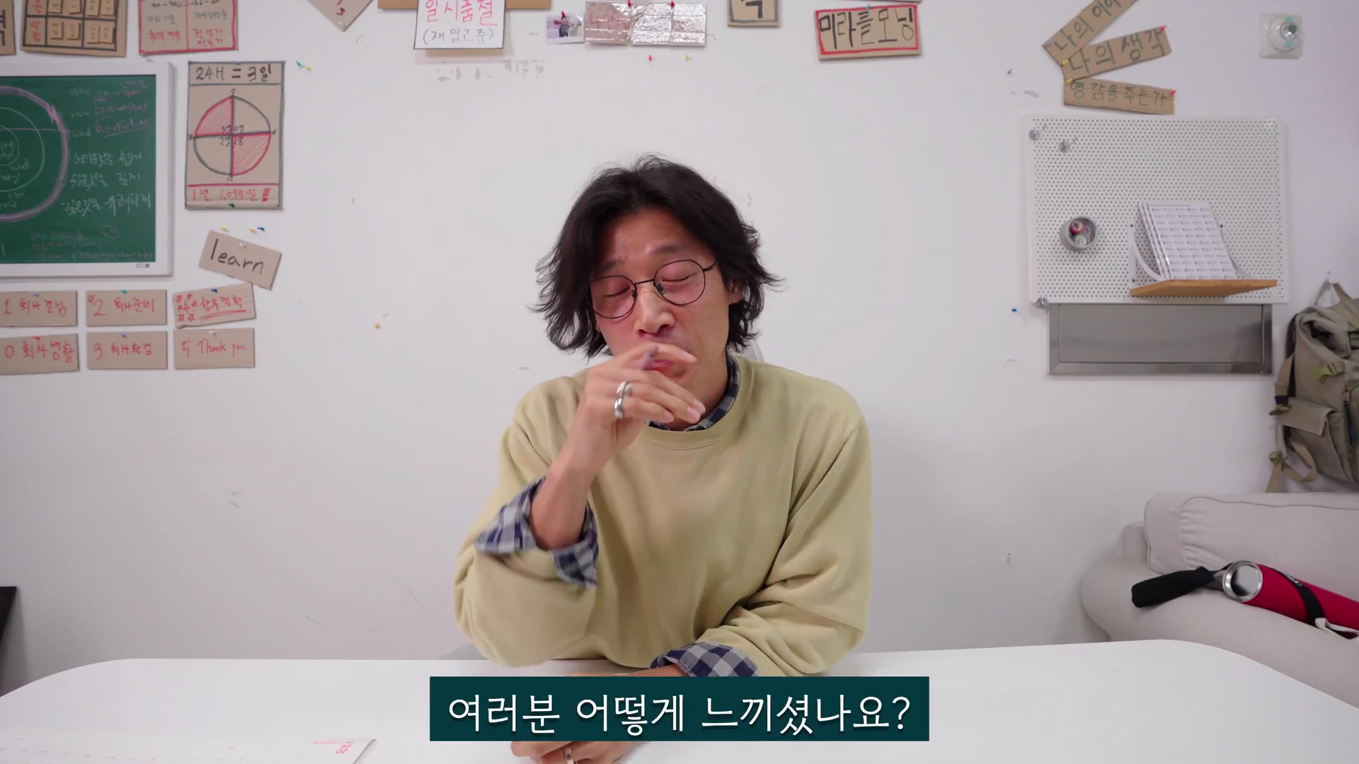 한 남성이 흰 벽을 배경으로 책상 앞에 앉아 눈을 감고 생각에 잠긴 듯 손을 입가에 대고 있는 모습.