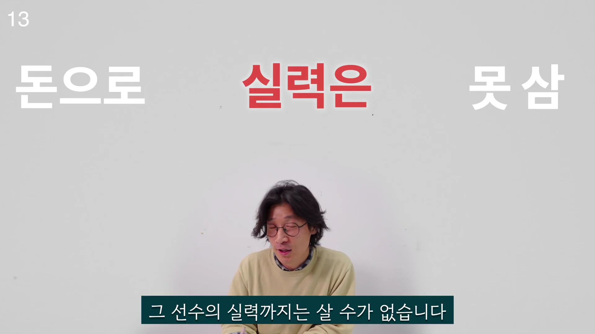 흰 배경 앞에 안경을 쓴 남성이 앉아 있고 화면 상단에 '돈으로 실력은 못 삼'이라는 문구가, 하단에 '그 선수의 실력까지는 살 수가 없습니다'라는 자막이 표시된 영상 화면.