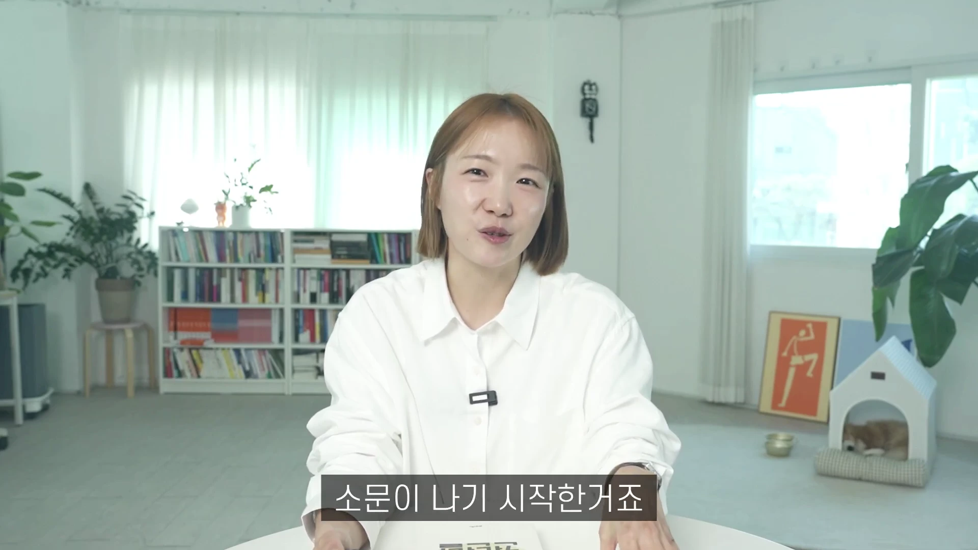 단발머리를 한 여성이 흰 셔츠를 입고 밝은 실내에서 이야기를 나누고 있는 모습입니다.