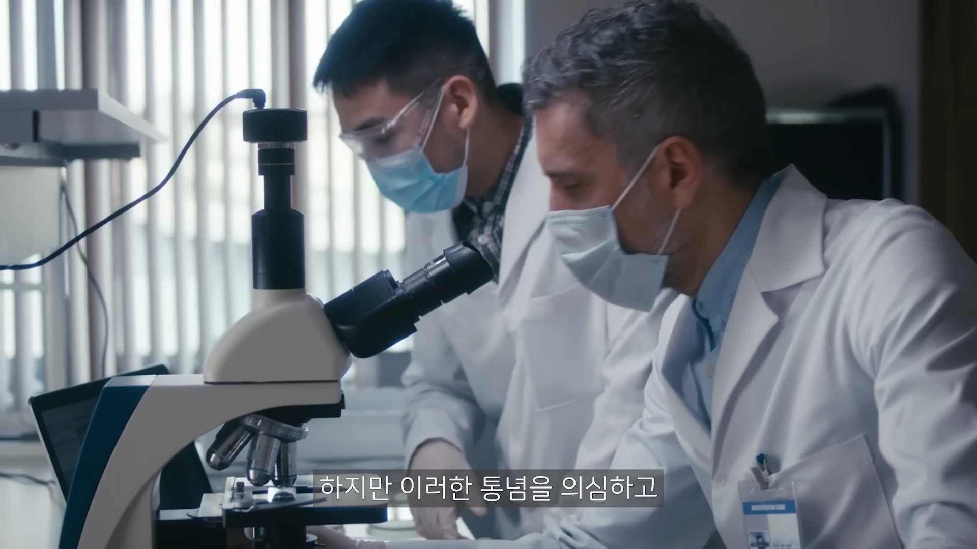 실험실 가운과 마스크를 착용한 두 연구원이 현미경을 들여다보며 실험하고 있는 모습이다.