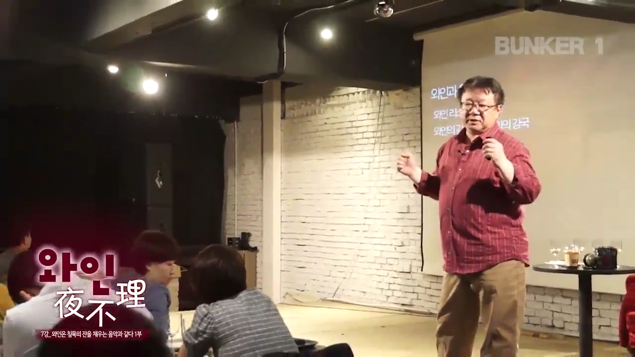 강연자가 무대 위에서 마이크를 잡고 관객을 향해 이야기를 전달하고 있으며, 뒤쪽 스크린에는 강연 주제가 텍스트로 투사되어 있습니다.