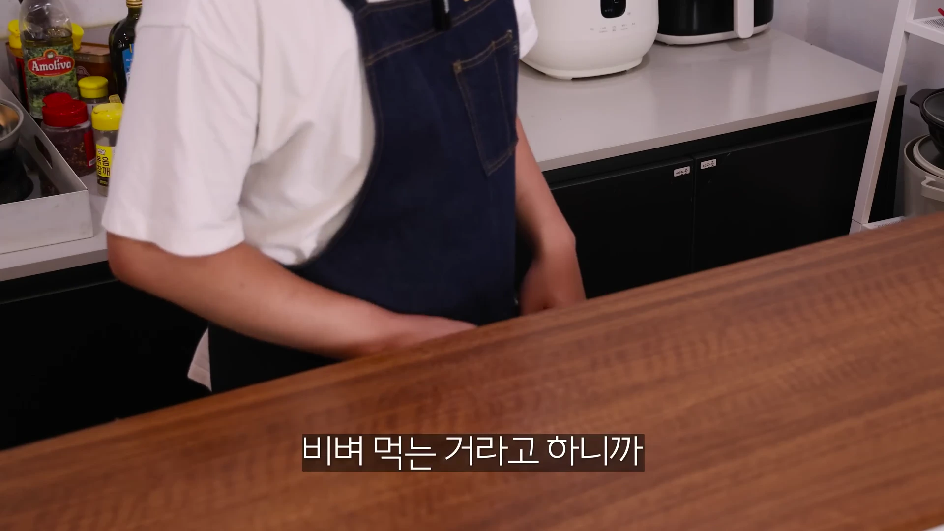 앞치마를 입은 요리사가 주방 조리대 앞에 서 있는 모습으로 화면 하단에는 자막이 떠 있다.