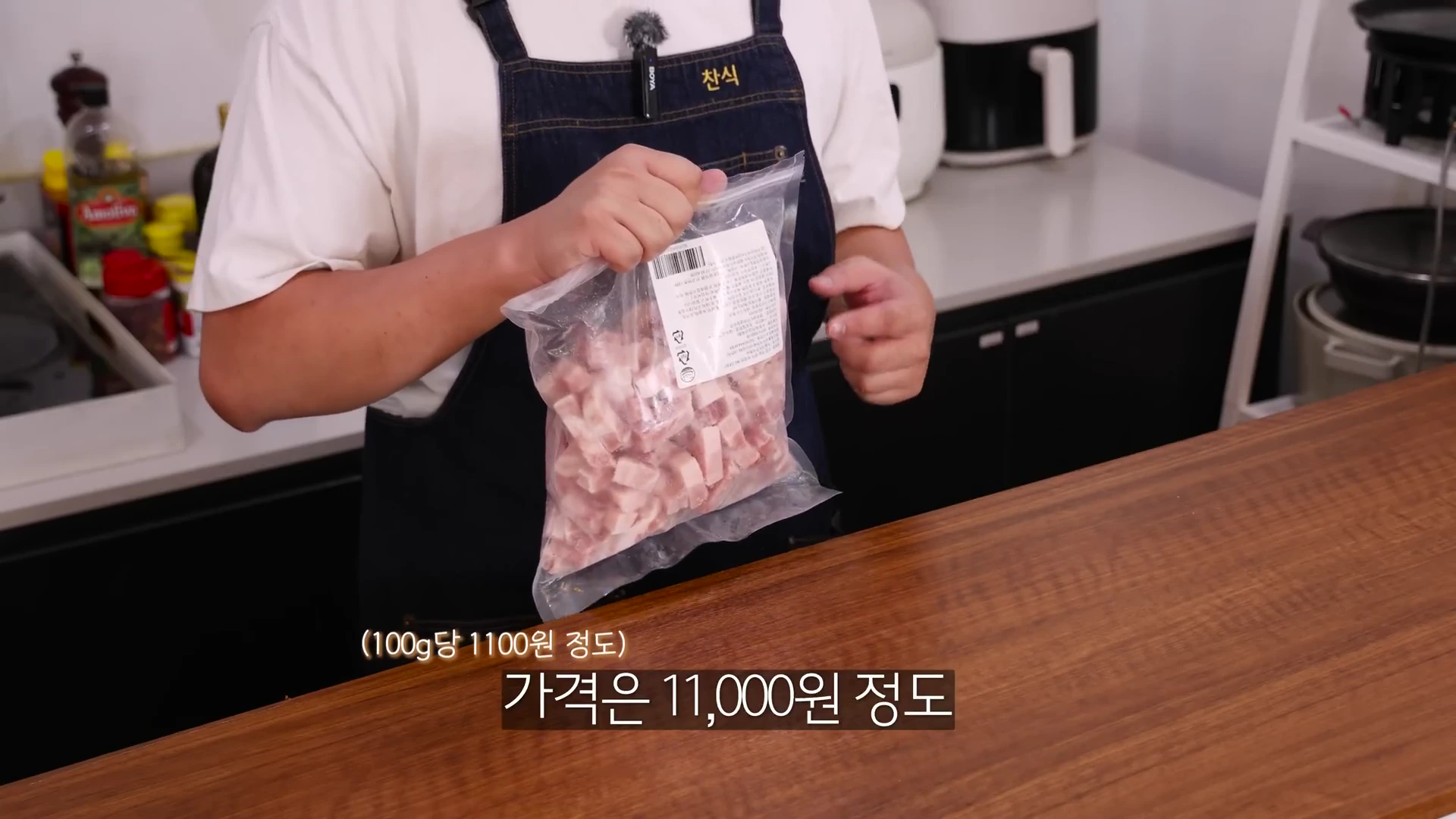 앞치마를 입은 요리사가 투명한 비닐에 든 한입 크기의 큐브 삼겹살 냉동 제품을 양손으로 들고 보여주는 모습