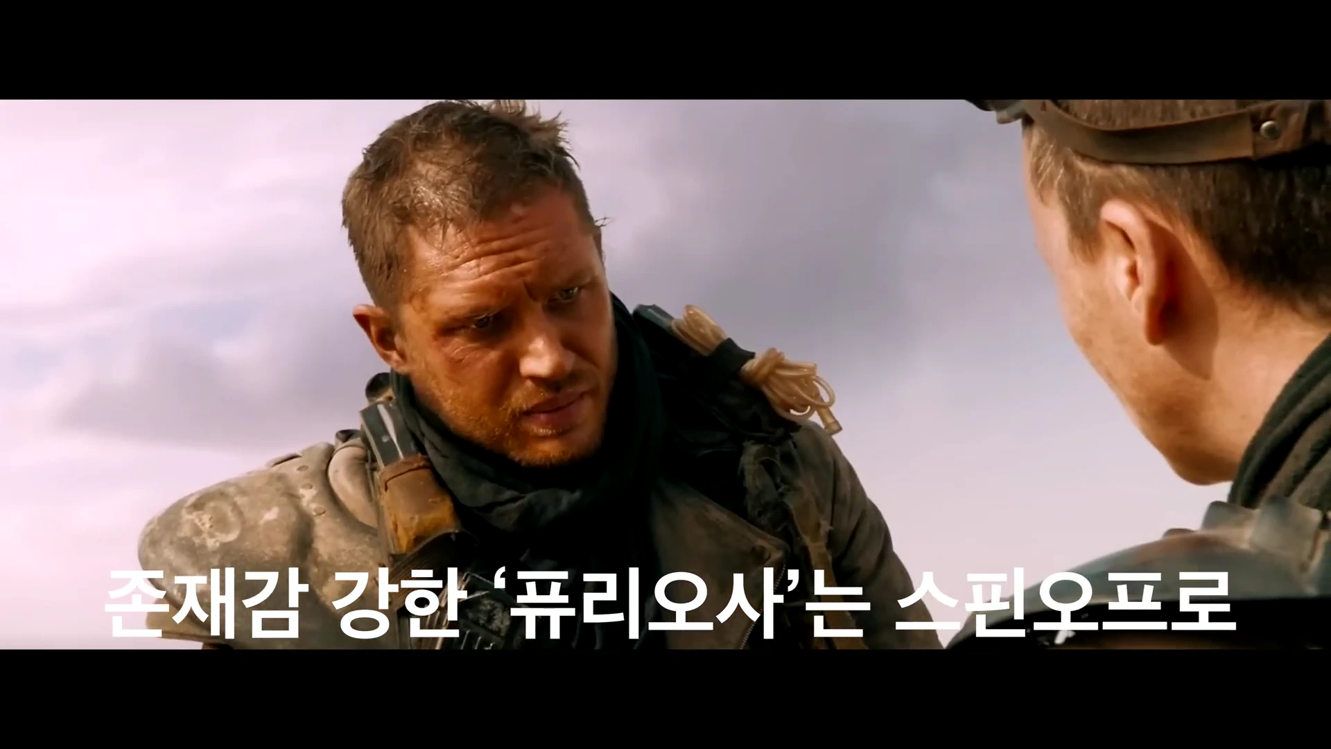 영화 속 거친 복장의 두 인물이 사막을 배경으로 서로를 마주 보고 대화하는 장면이 담긴 영상 캡처 화면