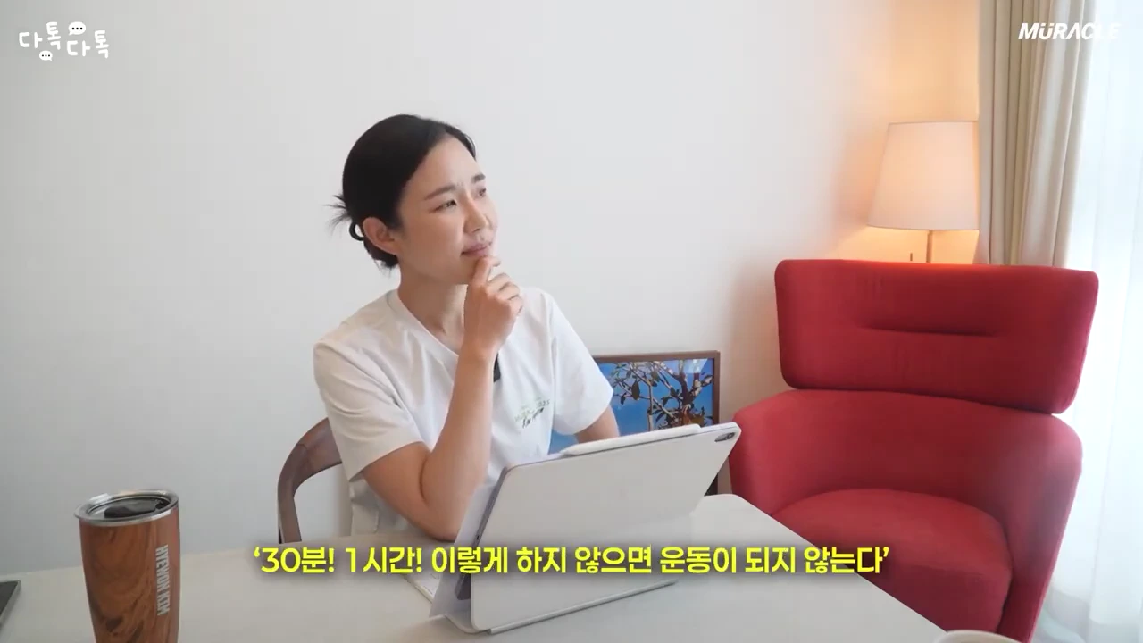 밝은 실내에서 흰 티셔츠를 입은 여성이 테이블 앞에 앉아 턱을 괸 채 생각에 잠긴 모습