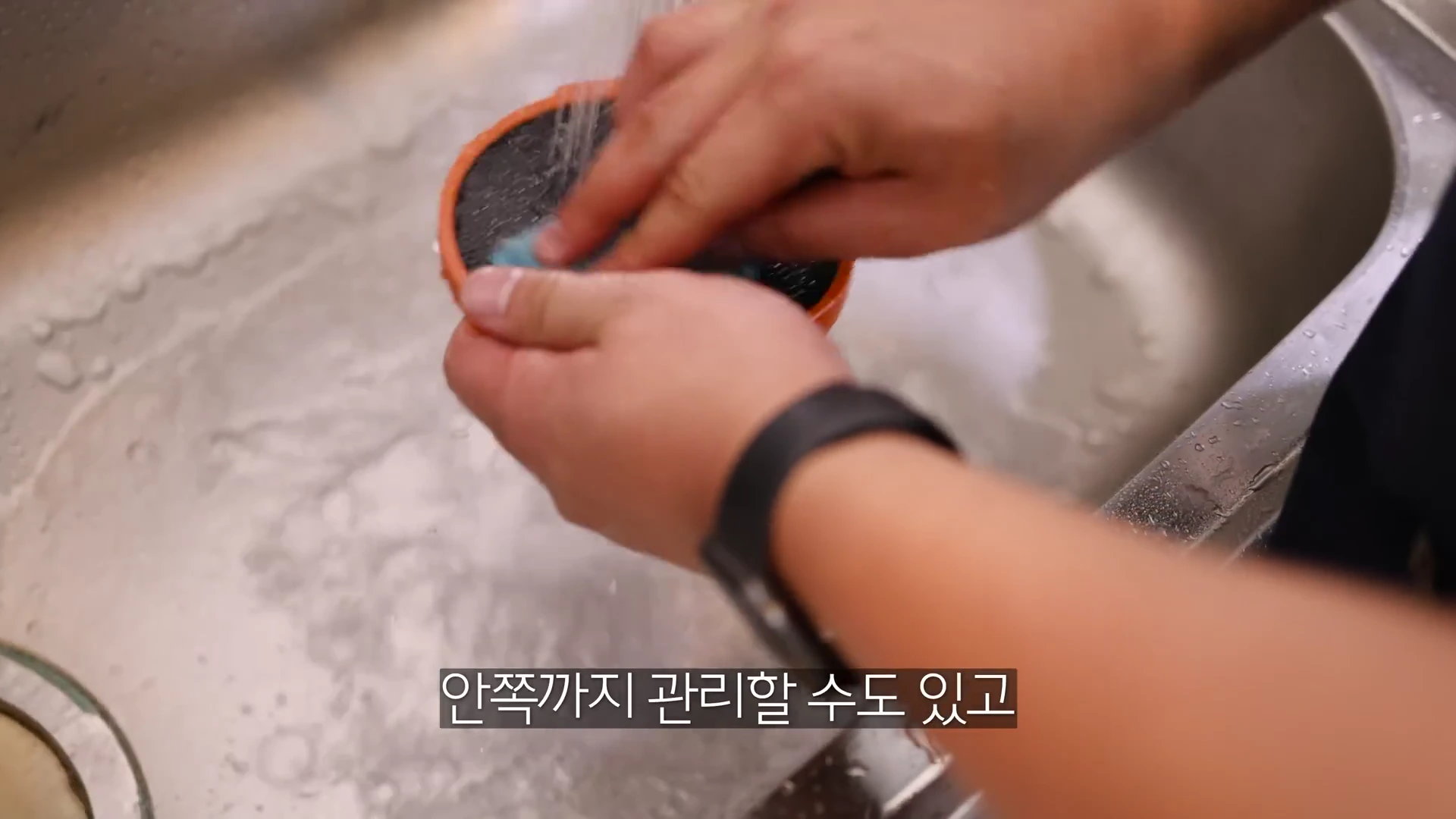 싱크대에서 손으로 주방 도구의 필터를 흐르는 물에 깨끗이 씻어내고 있는 모습.