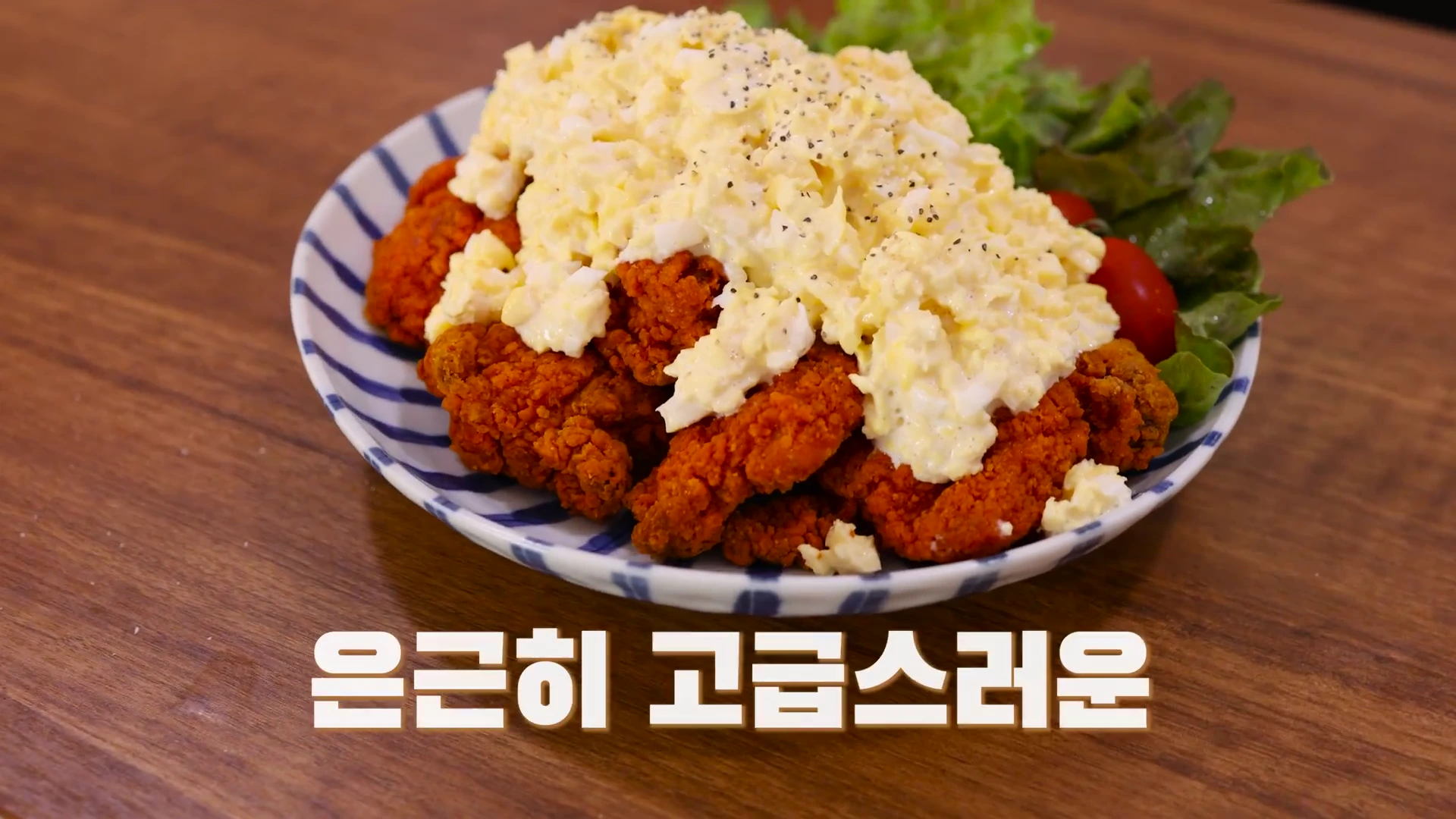 냉동 순살치킨 위에 노란 에그마요 타르타르 소스가 듬뿍 올려진 요리 접시. 옆에는 샐러드 채소와 방울토마토가 곁들여져 있고, 화면 하단에는 흰색 자막이 적혀 있음.