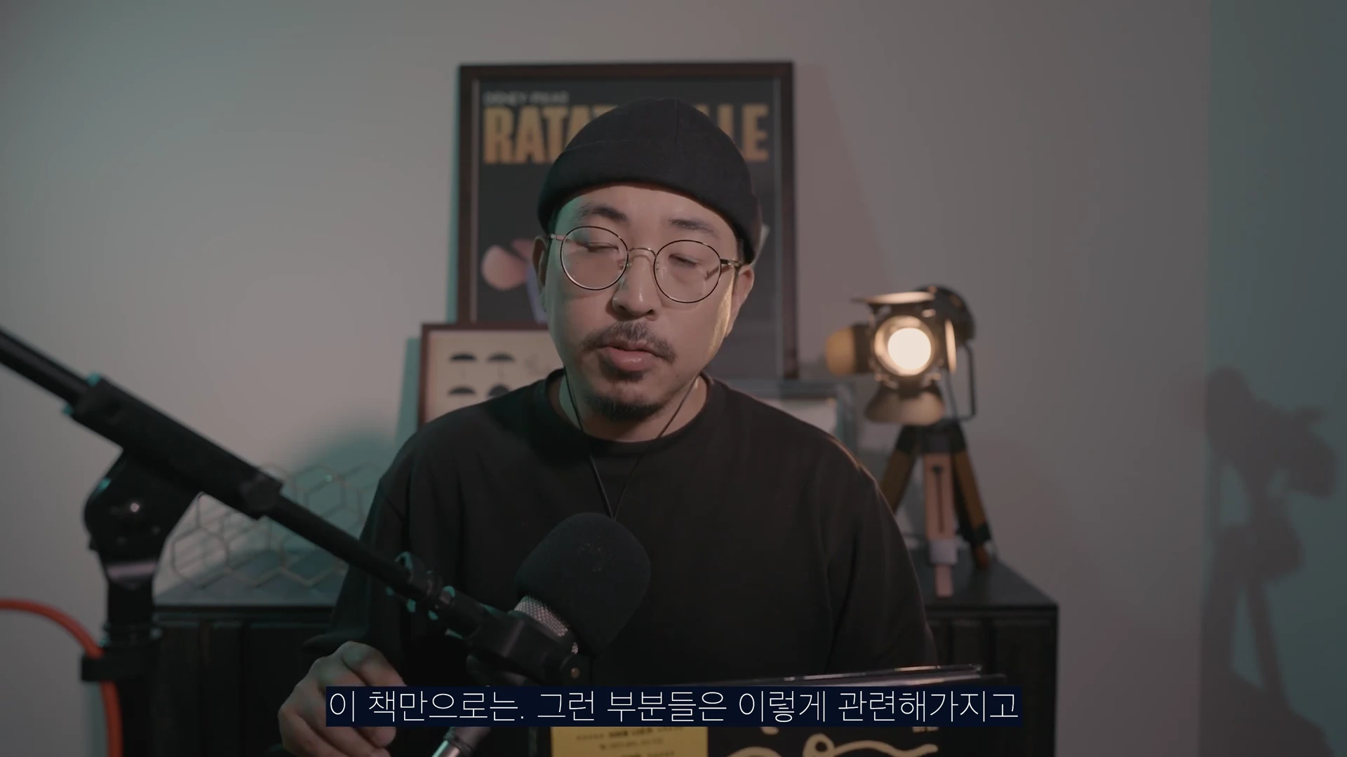 검은색 모자와 안경을 착용한 남성이 마이크 앞에서 진지한 표정으로 이야기하고 있는 모습의 영상 캡처 화면