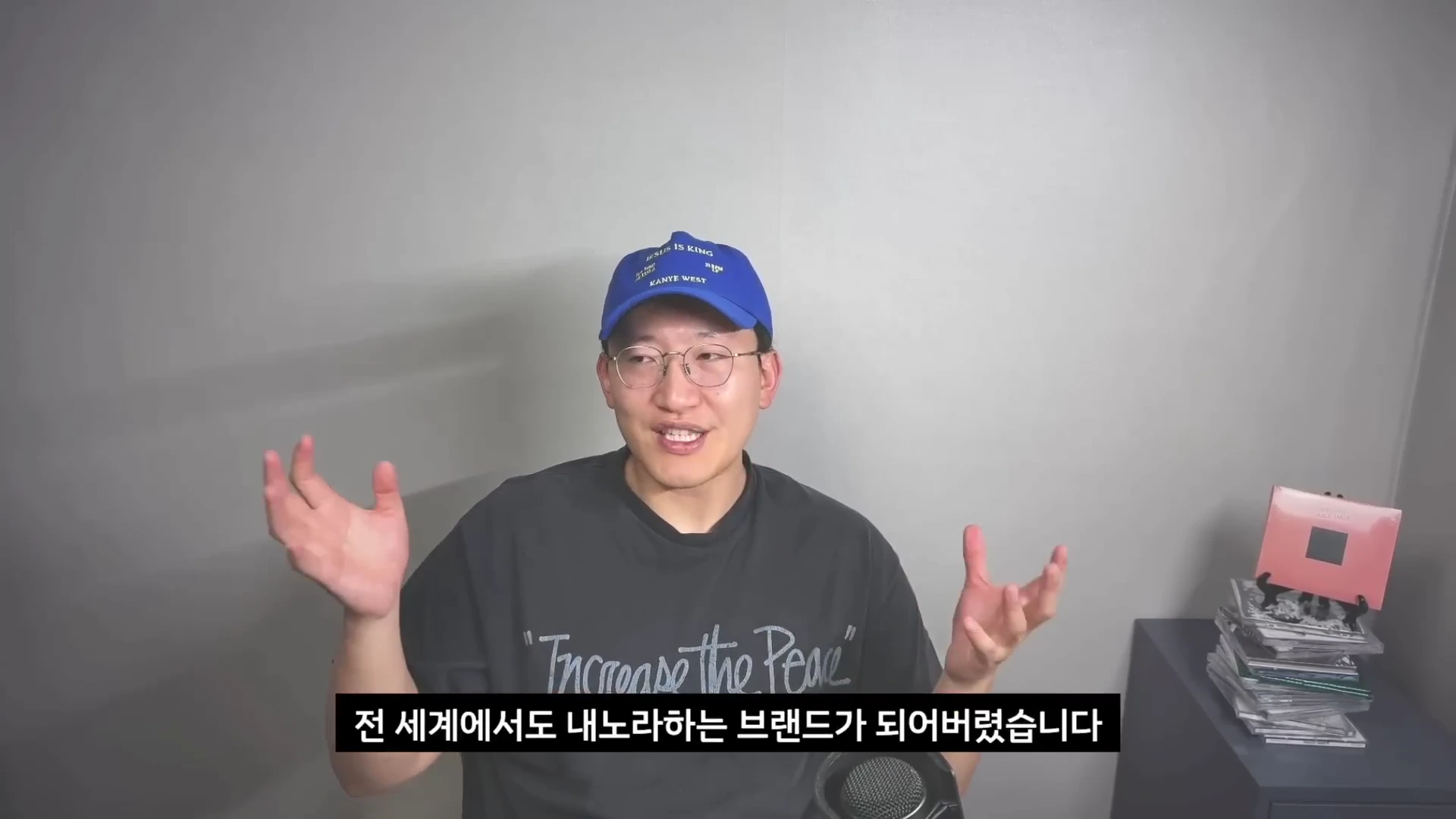 파란색 야구 모자를 쓰고 안경을 쓴 남성이 회색 배경 앞에서 양손을 벌려 이야기하고 있으며, 아래에는 한국어 자막이 표시된 영상 캡처 화면입니다.