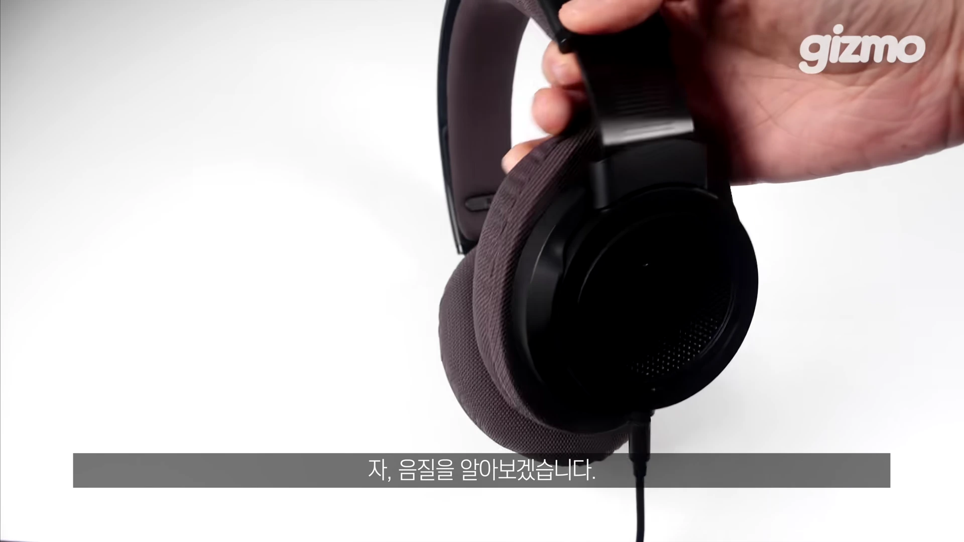사람의 손이 검은색 오픈형 유선 헤드폰의 헤어밴드 부분을 잡고 들어 올리고 있다.
