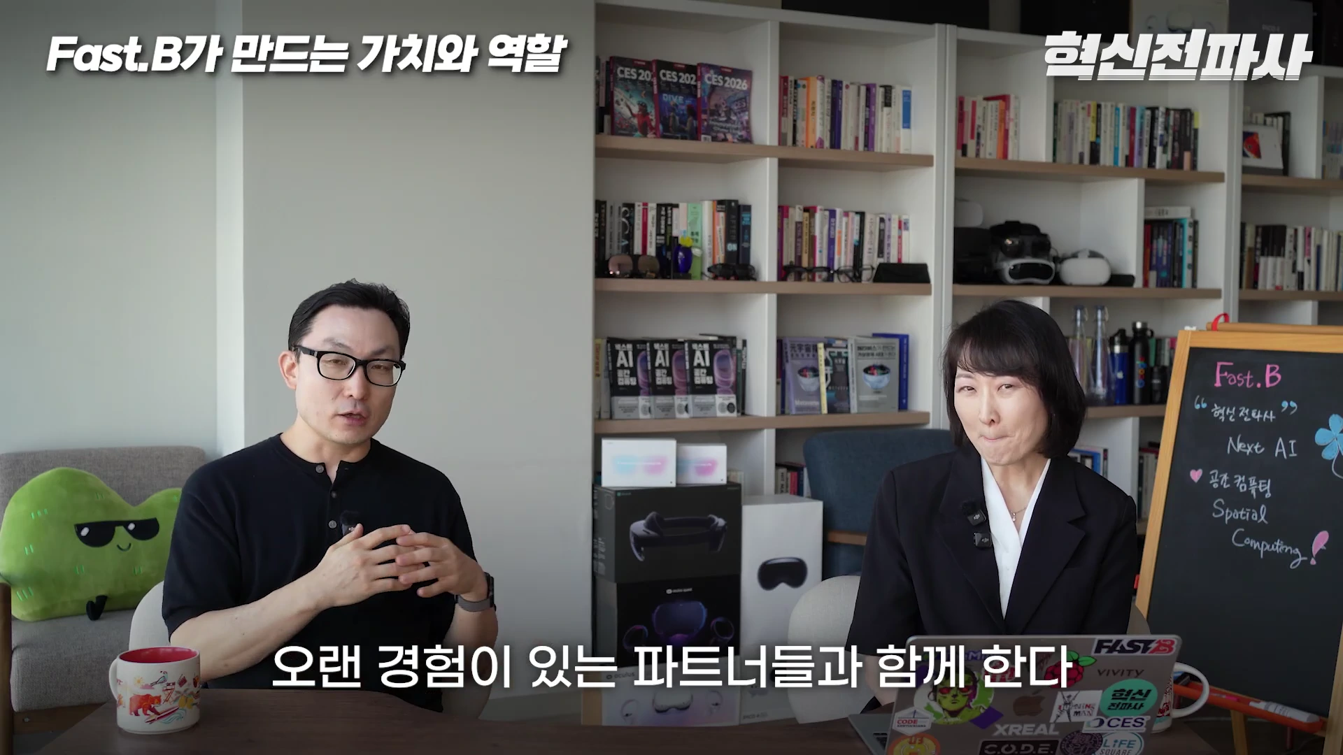 두 명의 출연자가 책장이 있는 실내에서 테이블 앞에 앉아 대화를 나누고 있으며, 옆에는 'Fast.B'라고 적힌 작은 칠판이 세워져 있습니다.