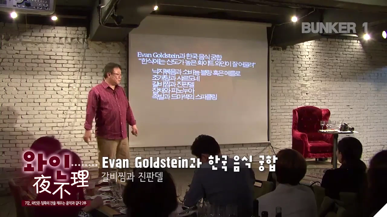 실내 강연장에서 한 남성이 스크린 앞에 서서 발표를 하고 있으며, 스크린에는 한국 음식과 와인의 궁합을 추천하는 텍스트가 표시되어 있습니다.