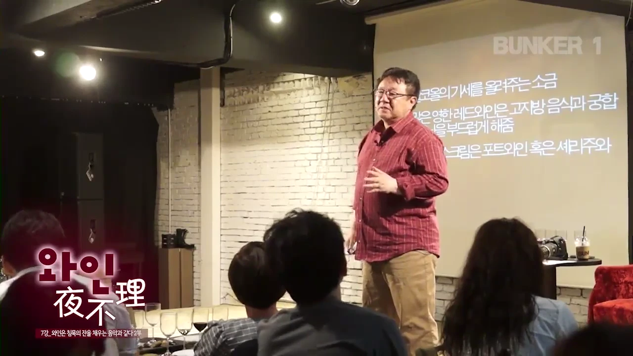 붉은 체크무늬 셔츠를 입은 남성이 강단에 서서 청중을 향해 설명하고 있고, 뒤편 스크린에는 와인 페어링 팁이 적힌 자막이 투사되고 있습니다.