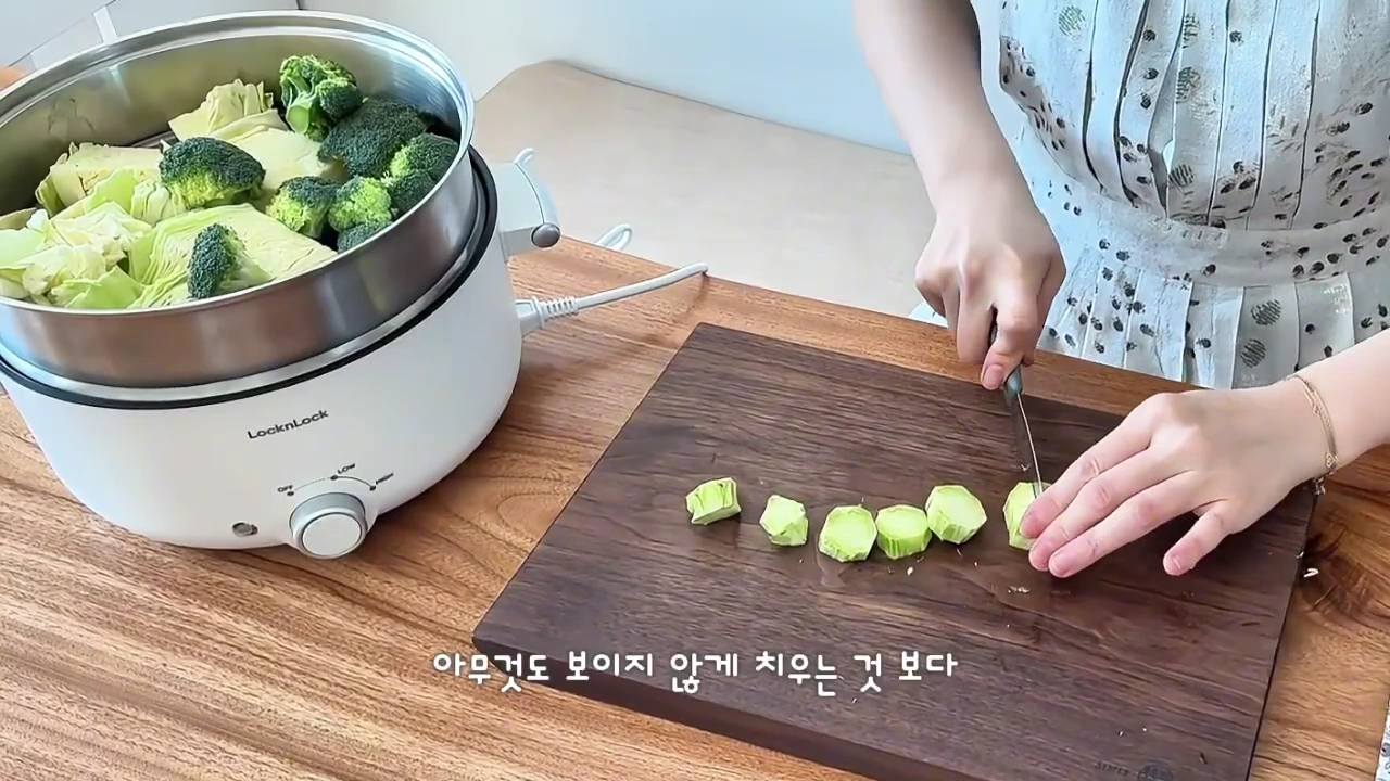 한 사람이 도마 위에서 식재료를 손질하고 있으며 옆에는 찜기가 놓여 있다.