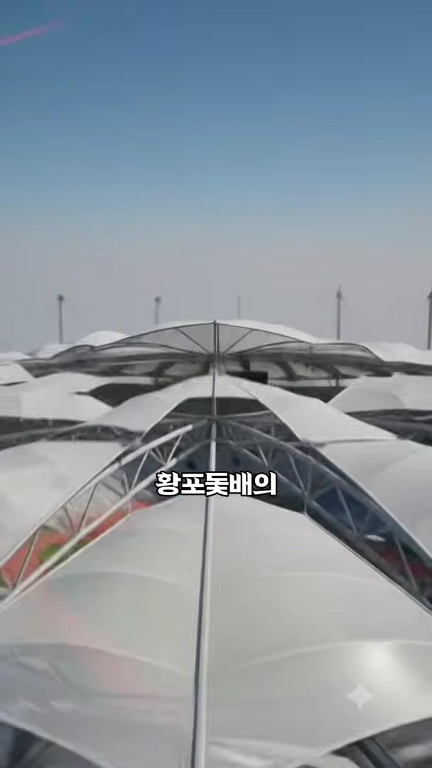 상암 경기장의 반투명한 지붕 구조가 겹겹이 펼쳐져 있고 배경에는 얇고 높은 마스트들이 하늘을 향해 솟아 있는 모습