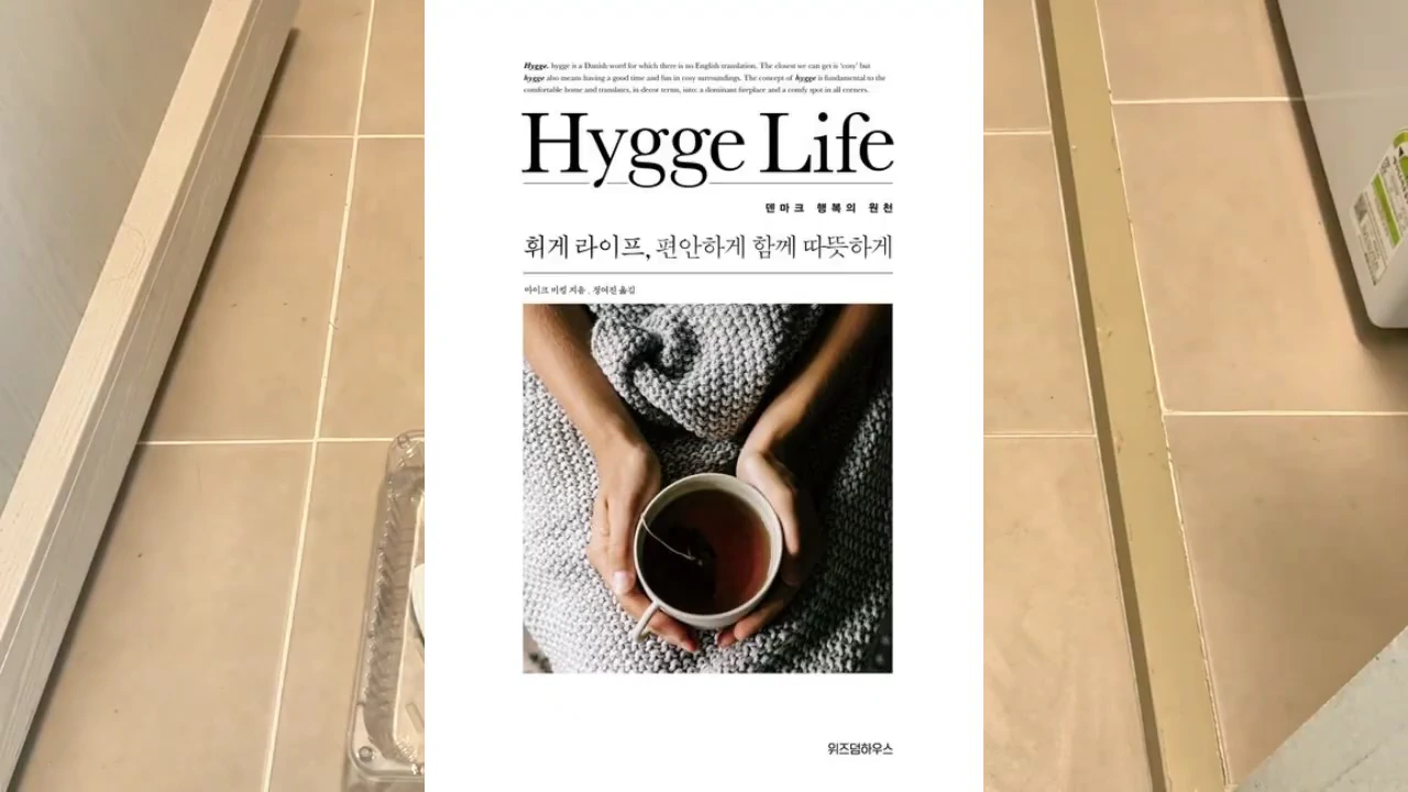 '휘게 라이프'라는 제목이 적힌 책 표지에 차를 든 두 손과 따뜻한 니트 소재의 배경이 담겨 있다.