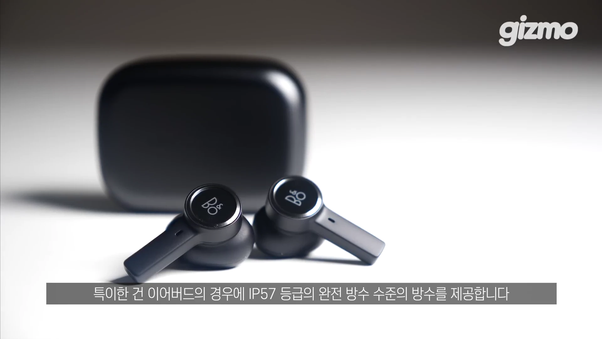 검은색 무선 이어폰 한 쌍과 그 뒤에 놓인 충전 케이스가 흰색 배경 위에 놓여 있습니다.