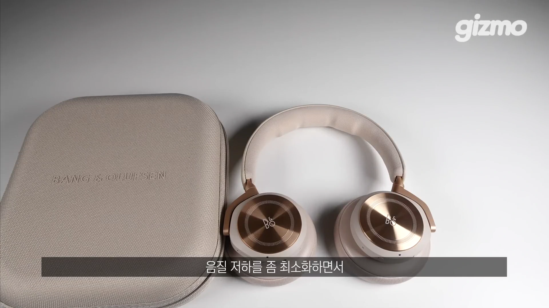 밝은 톤의 뱅앤올룹슨 무선 헤드폰과 전용 휴대용 케이스가 흰색 배경 위에 나란히 놓여 있습니다.