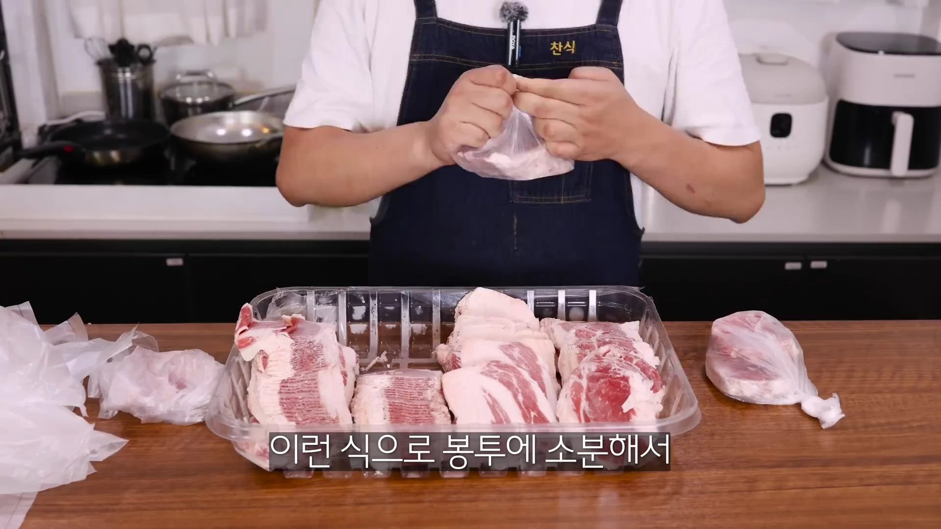 앞치마를 두른 요리사가 대용량 플라스틱 용기에 담긴 냉동 차돌박이를 비닐봉투에 일인분씩 나누어 담고 있다.
