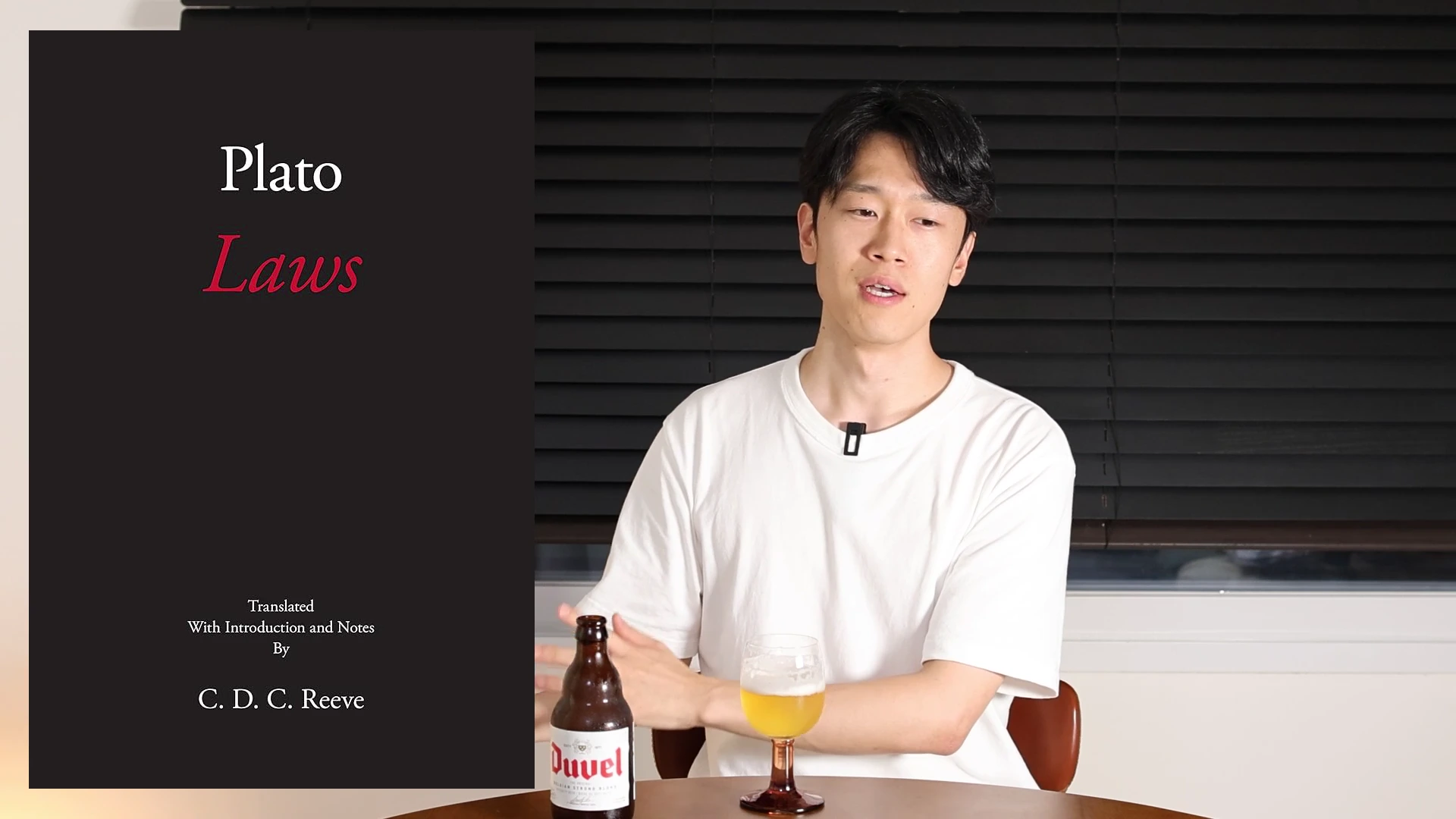 흰색 티셔츠를 입은 남성이 책상 앞에 앉아 이야기하고 있고, 화면 왼쪽에는 'Plato Laws'라는 제목의 책 표지가 그래픽으로 삽입되어 있으며 테이블 위에는 맥주 병과 잔이 놓여 있습니다.