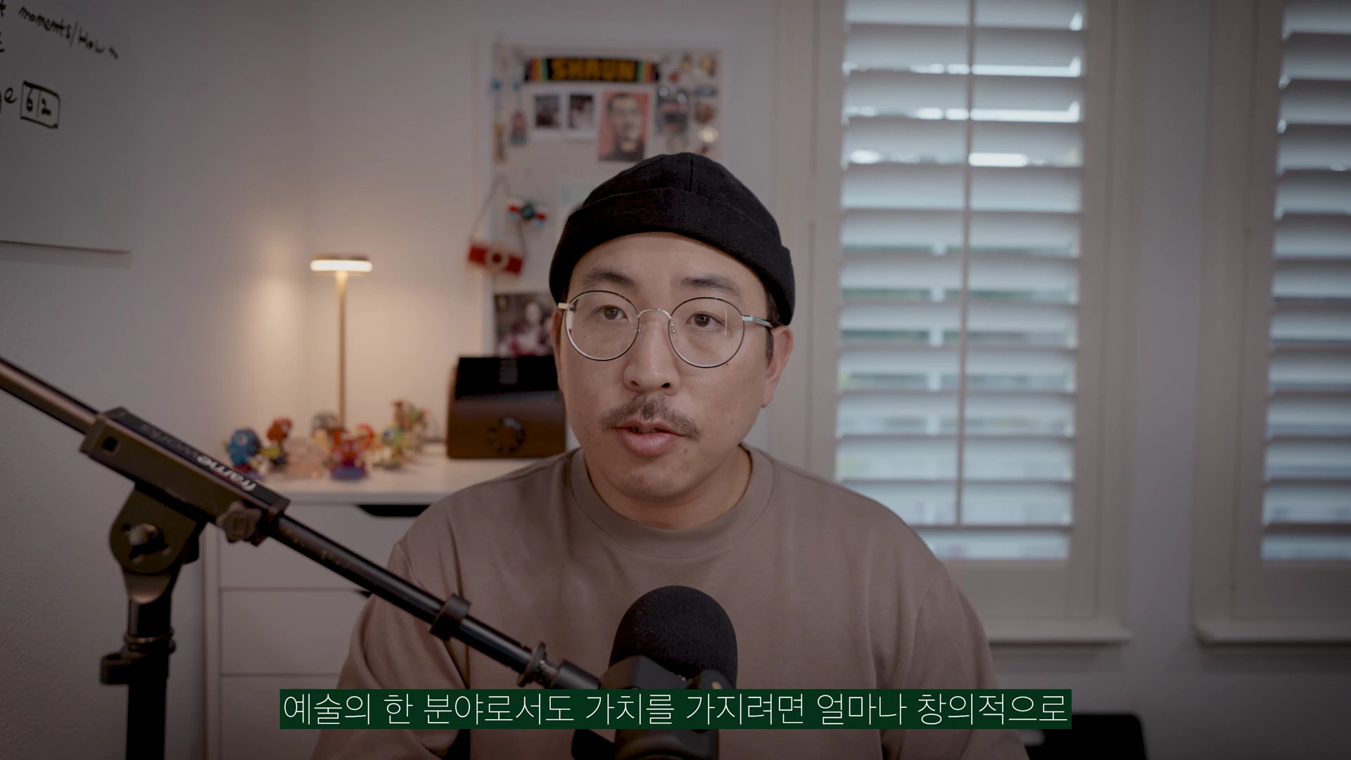 안경을 쓰고 검은색 비니를 쓴 남성이 마이크 앞에 앉아 정면을 응시하며 이야기하는 스튜디오 촬영 화면