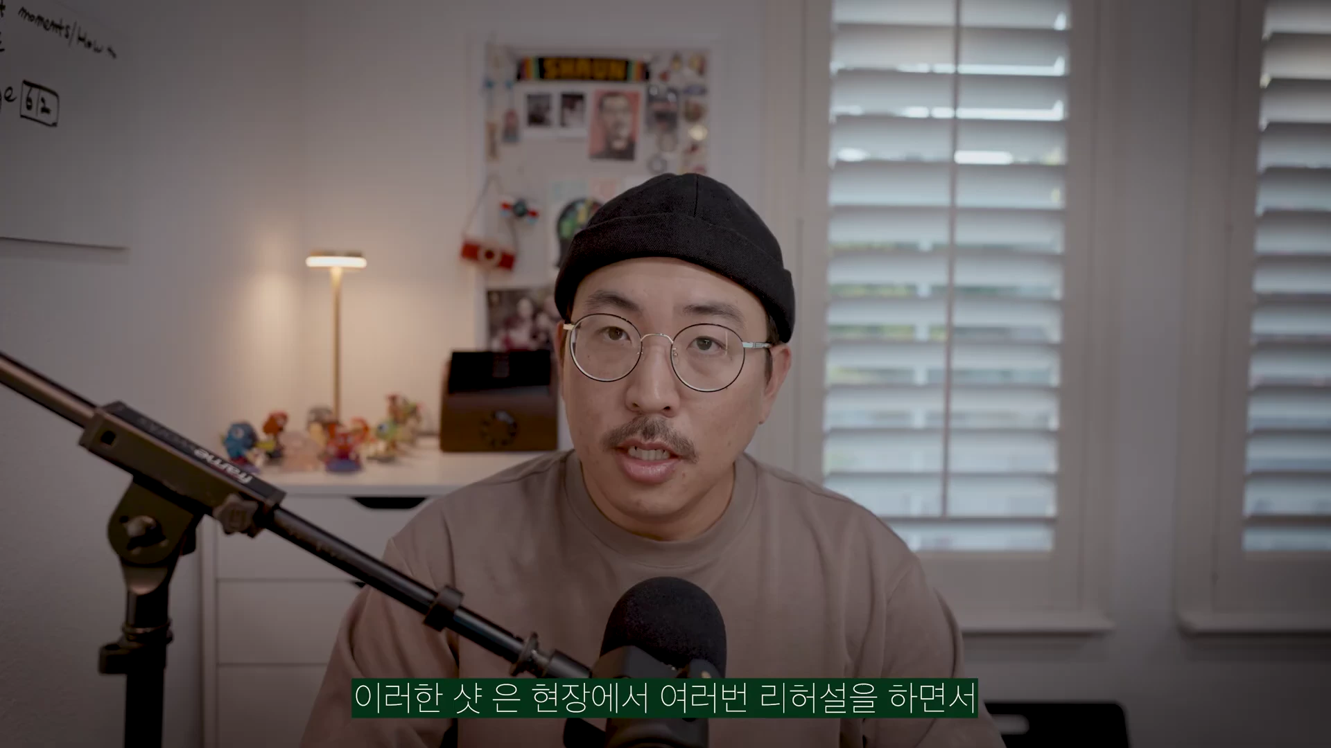 안경을 쓰고 검은색 비니를 착용한 남성이 마이크 앞에서 이야기하고 있으며, 화면 하단에는 한국어 자막이 표시되어 있습니다.