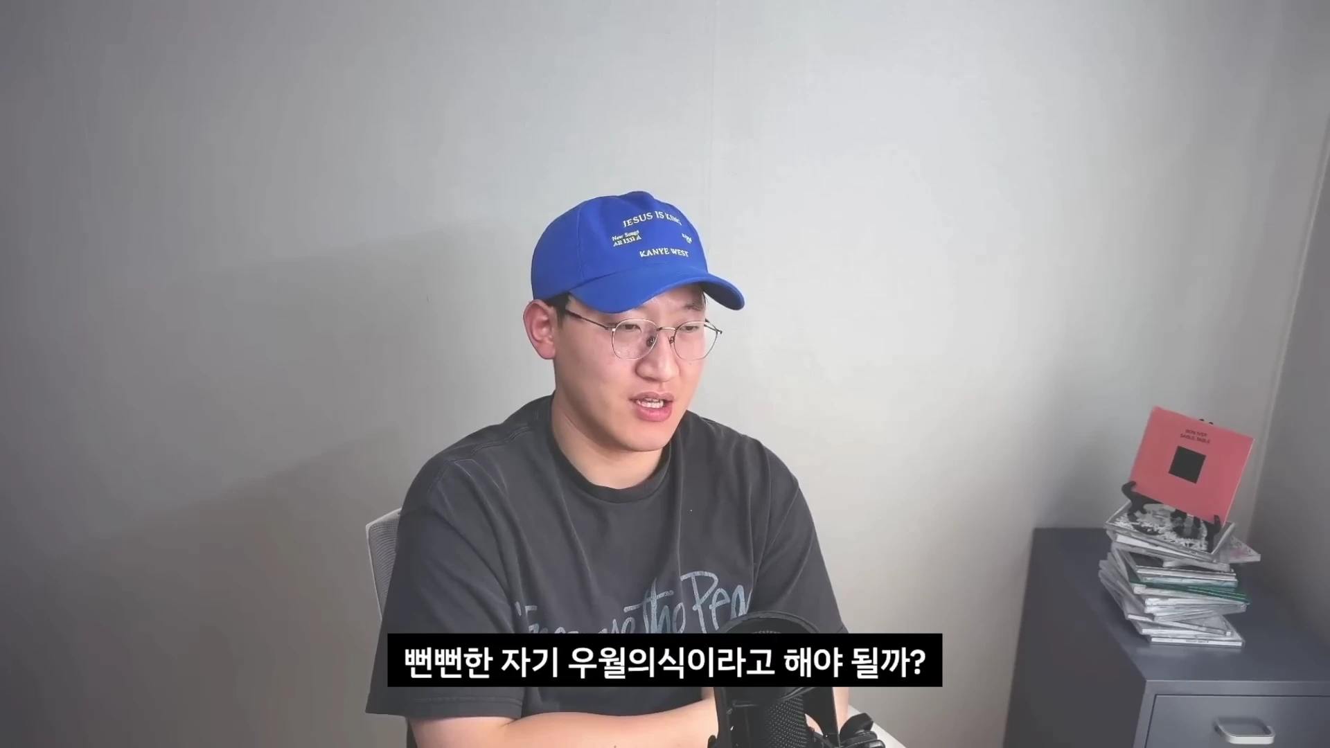 파란색 야구 모자와 안경을 쓴 남성이 마이크 앞에서 이야기하고 있으며 하단에는 '뻔뻔한 자기 우월의식이라고 해야 될까?'라는 자막이 표시되어 있다.