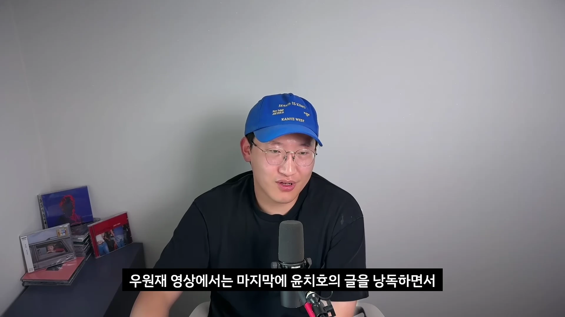 파란색 야구 모자를 쓰고 안경을 쓴 남성이 마이크 앞에서 이야기를 하고 있는 모습입니다.