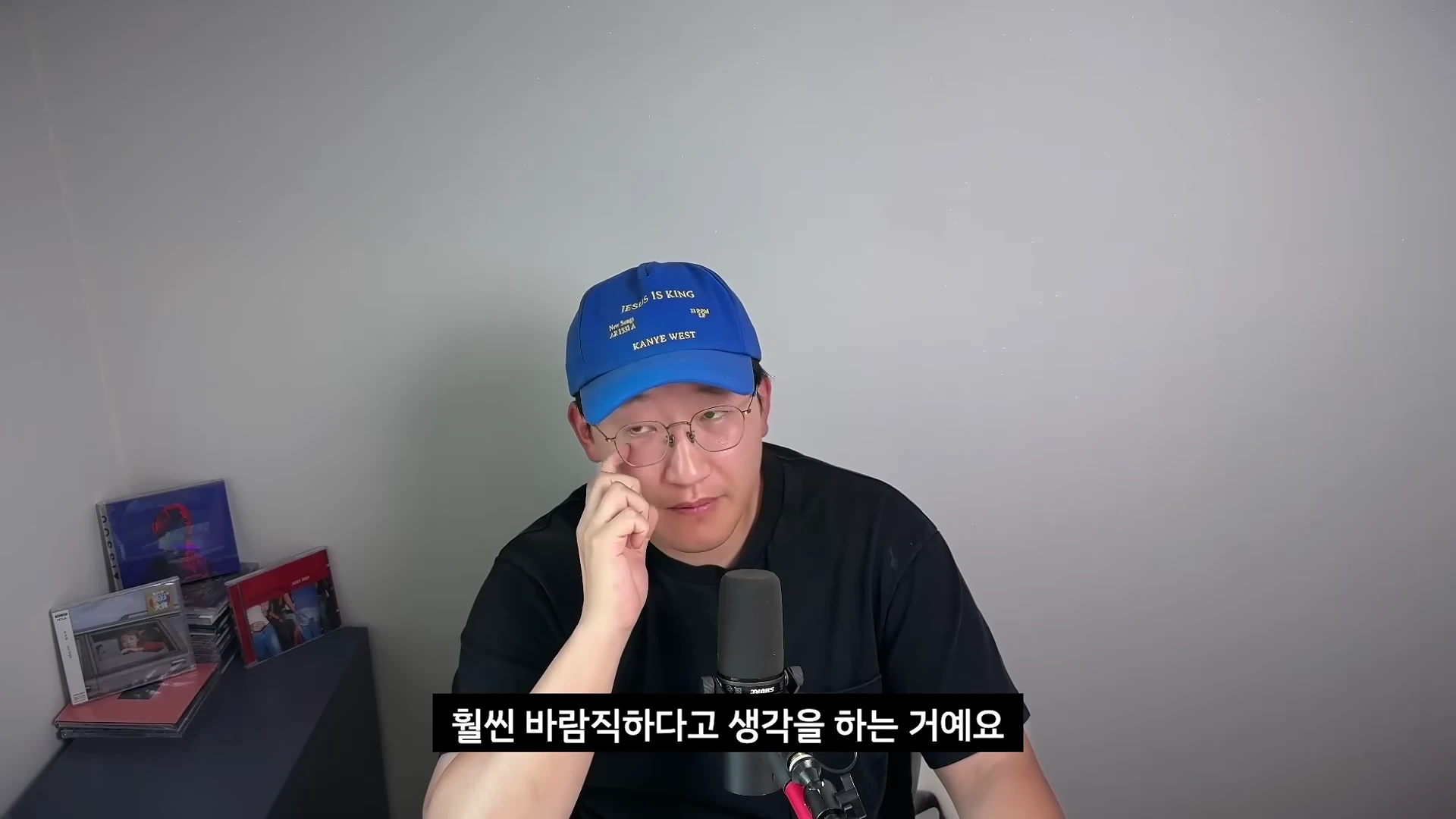 파란색 야구 모자와 안경을 착용한 남성이 마이크 앞에서 진지한 표정으로 이야기를 나누고 있다.