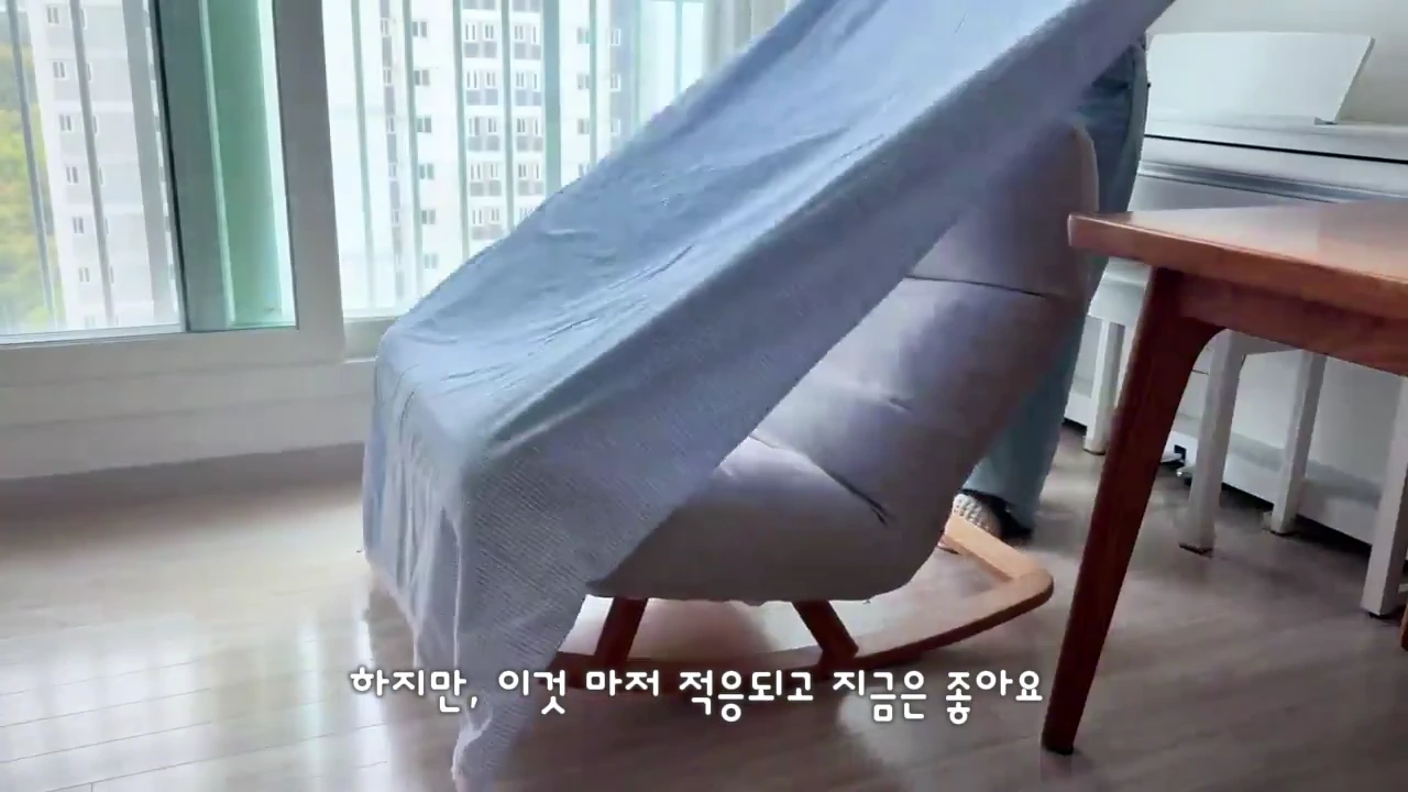 실내에서 사람이 1인용 흔들의자 위에 밝은 색 천을 덮고 있는 모습